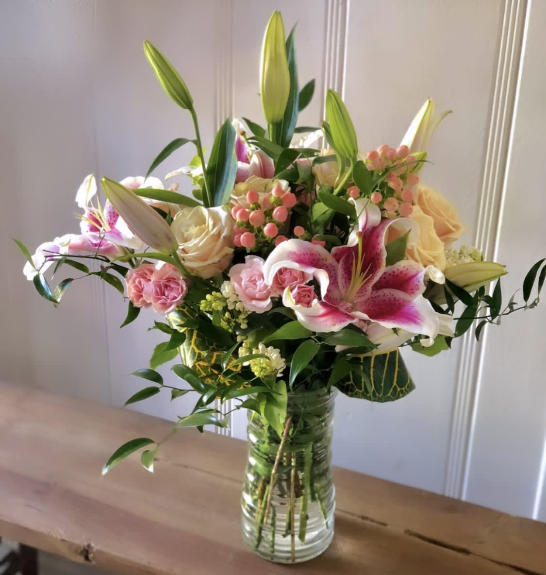 Mixed bouquet of pink lilies, roses, and spray roses in a clear glass vase