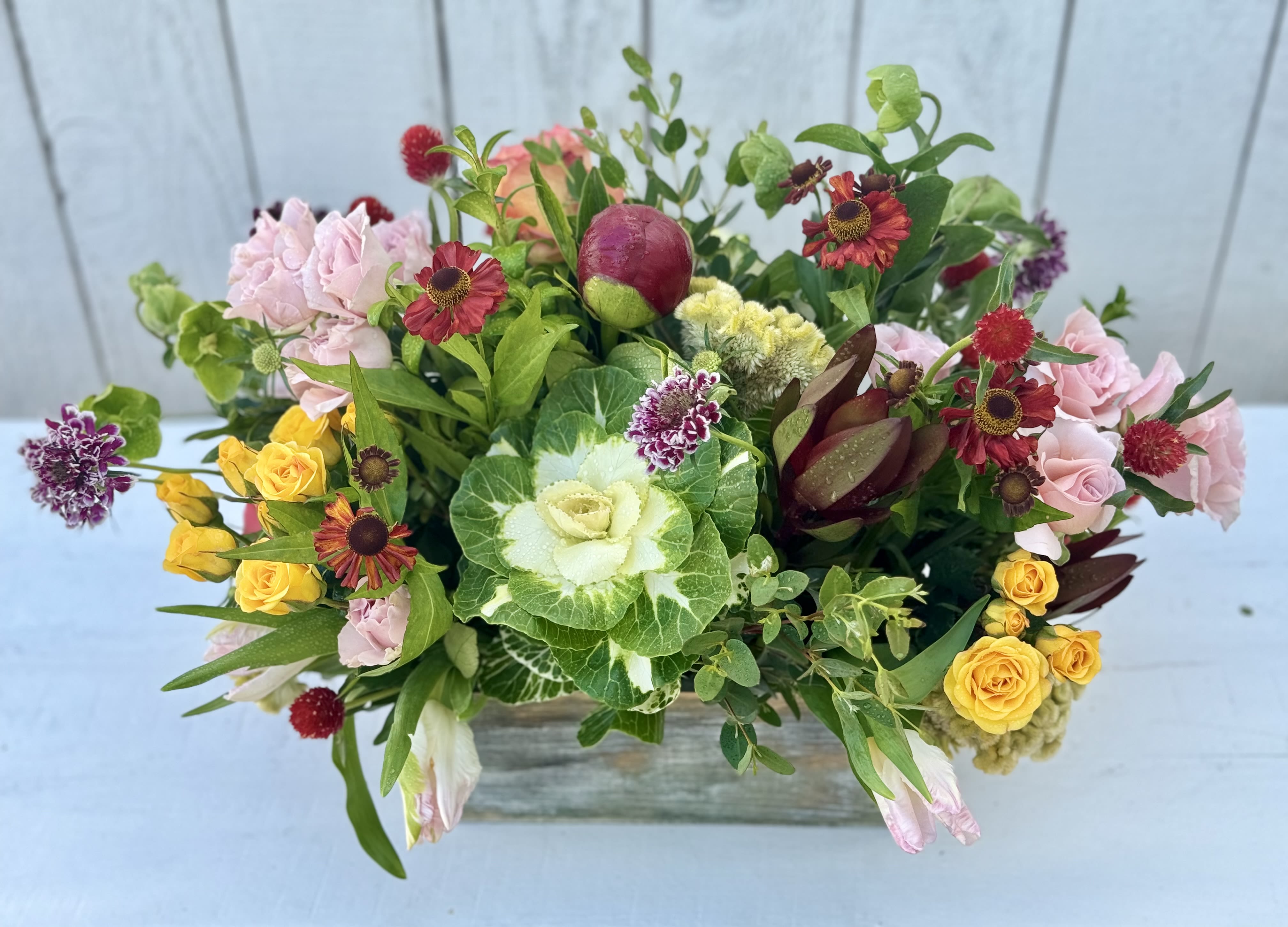 Mixed bouquet with pink and yellow roses in a low wooden container