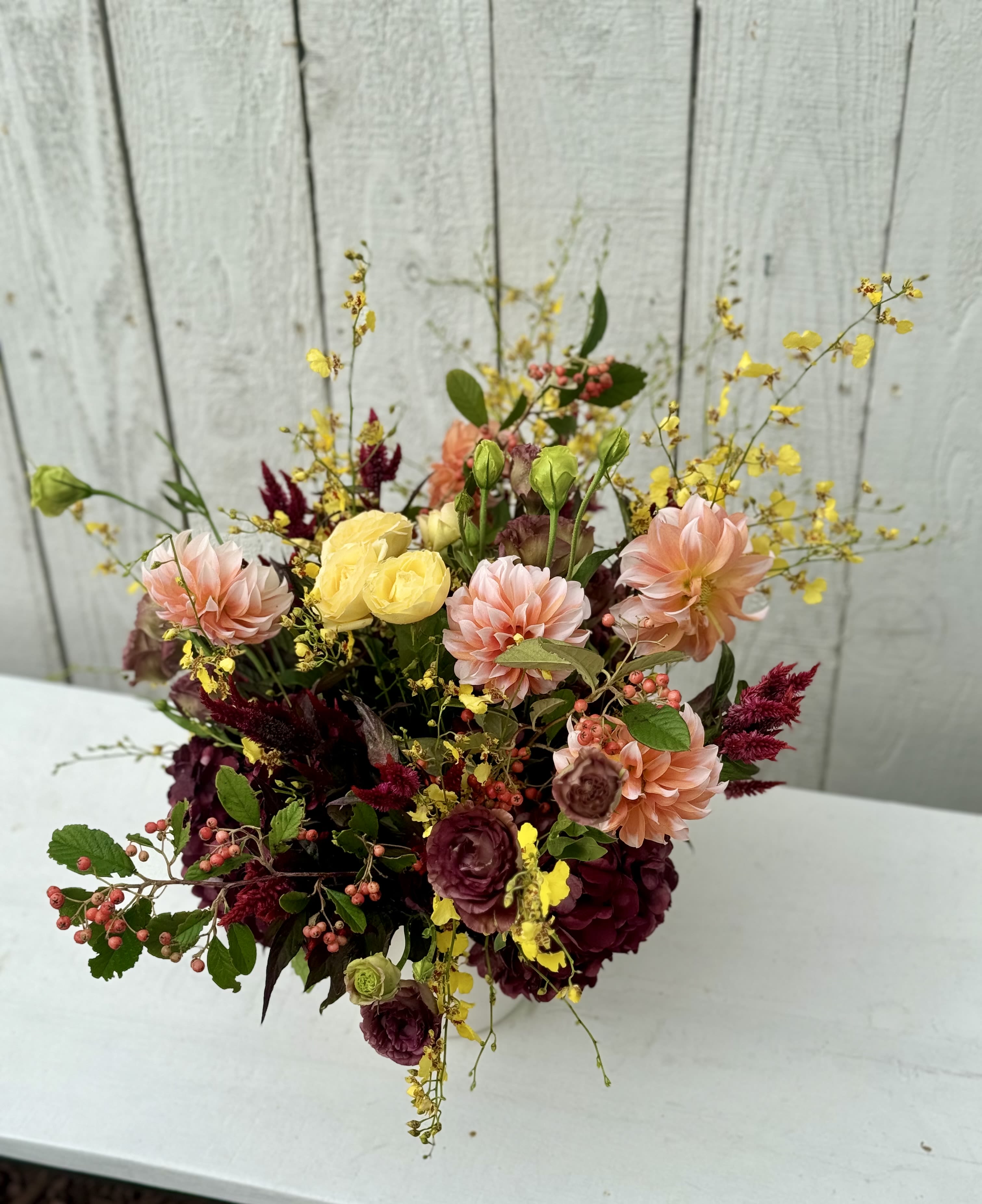 Mixed bouquet with peach, yellow, and burgundy flowers in a vase