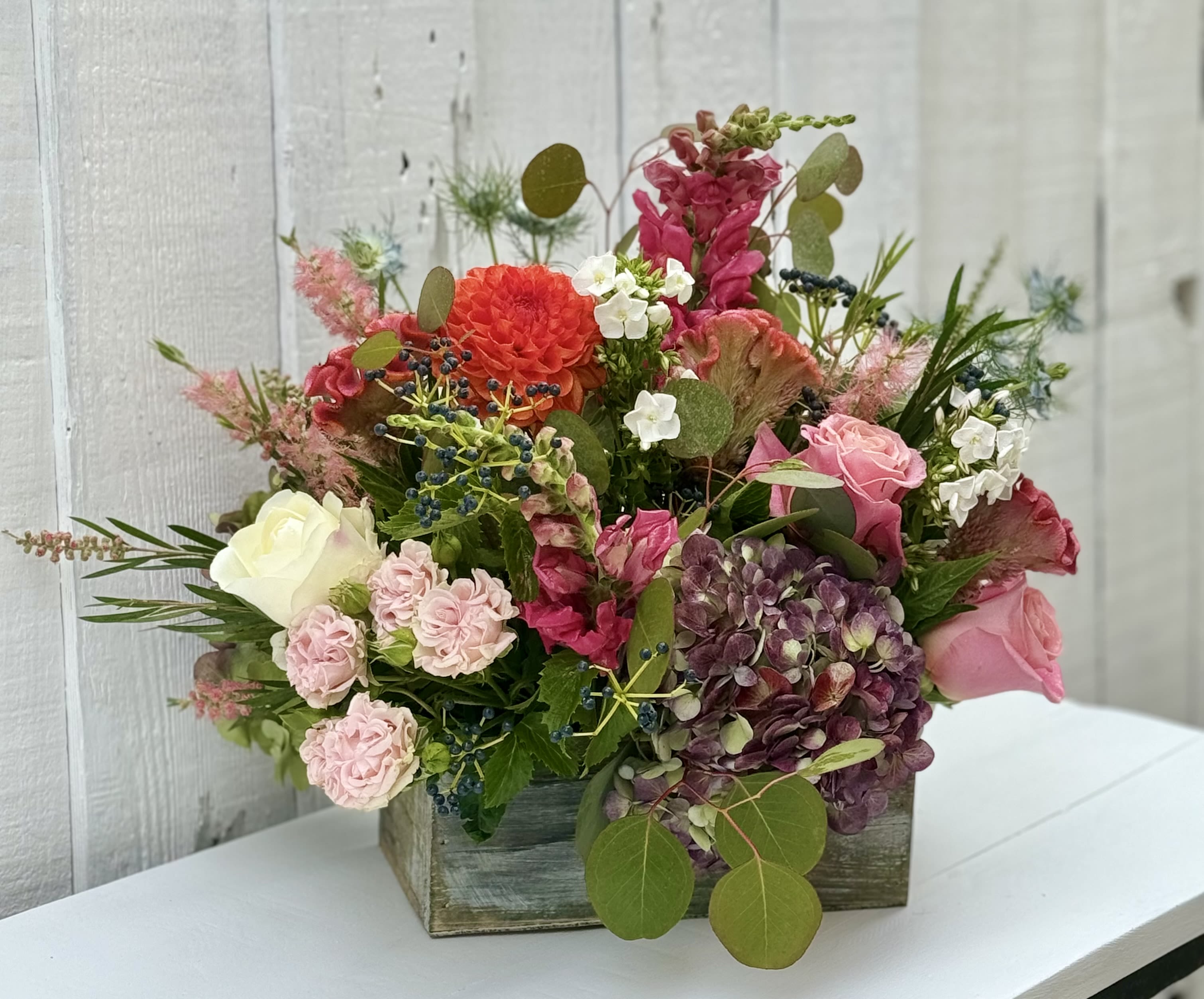 Mixed floral arrangement in a wooden box with pink, white, and purple blooms
