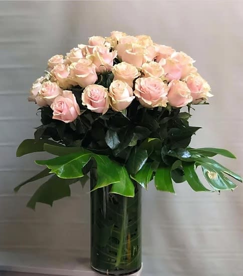 Pink roses arranged in a tall glass vase with broad green leaves