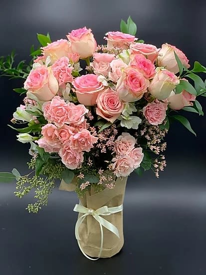 Pink roses and carnations arranged in a wrapped bouquet with a ribbon