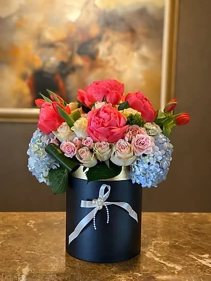 Pink and blue floral arrangement in a dark round box with a ribbon