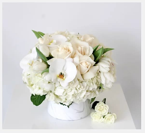 White roses and orchids arranged in a white box with green leaves