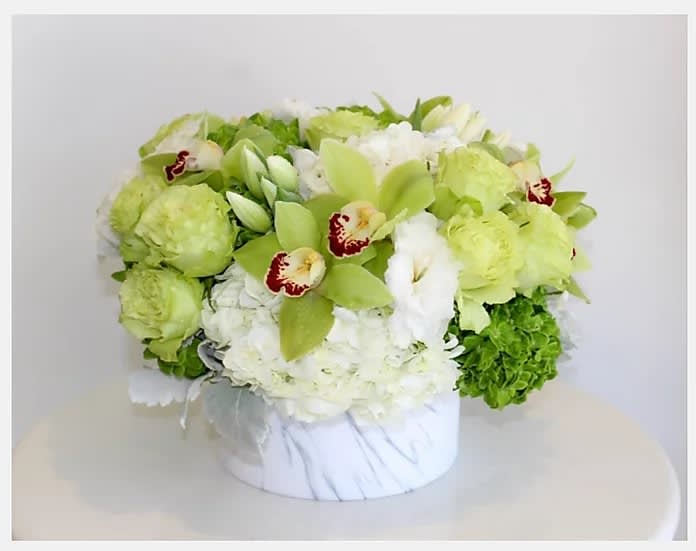Green and white floral arrangement in a round white box