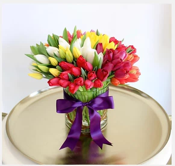 Colorful tulip bouquet in a glass vase with a purple ribbon