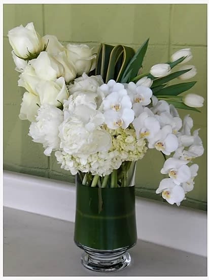 White floral arrangement in a tall green glass vase
