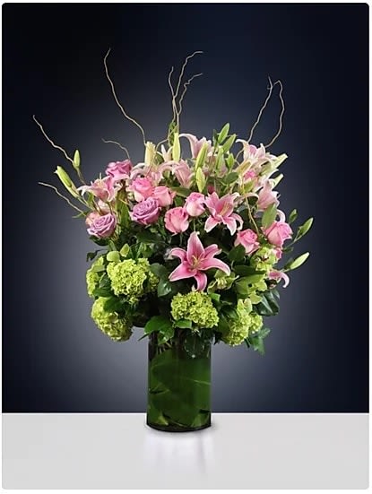 Pink lilies and roses in a tall green glass vase