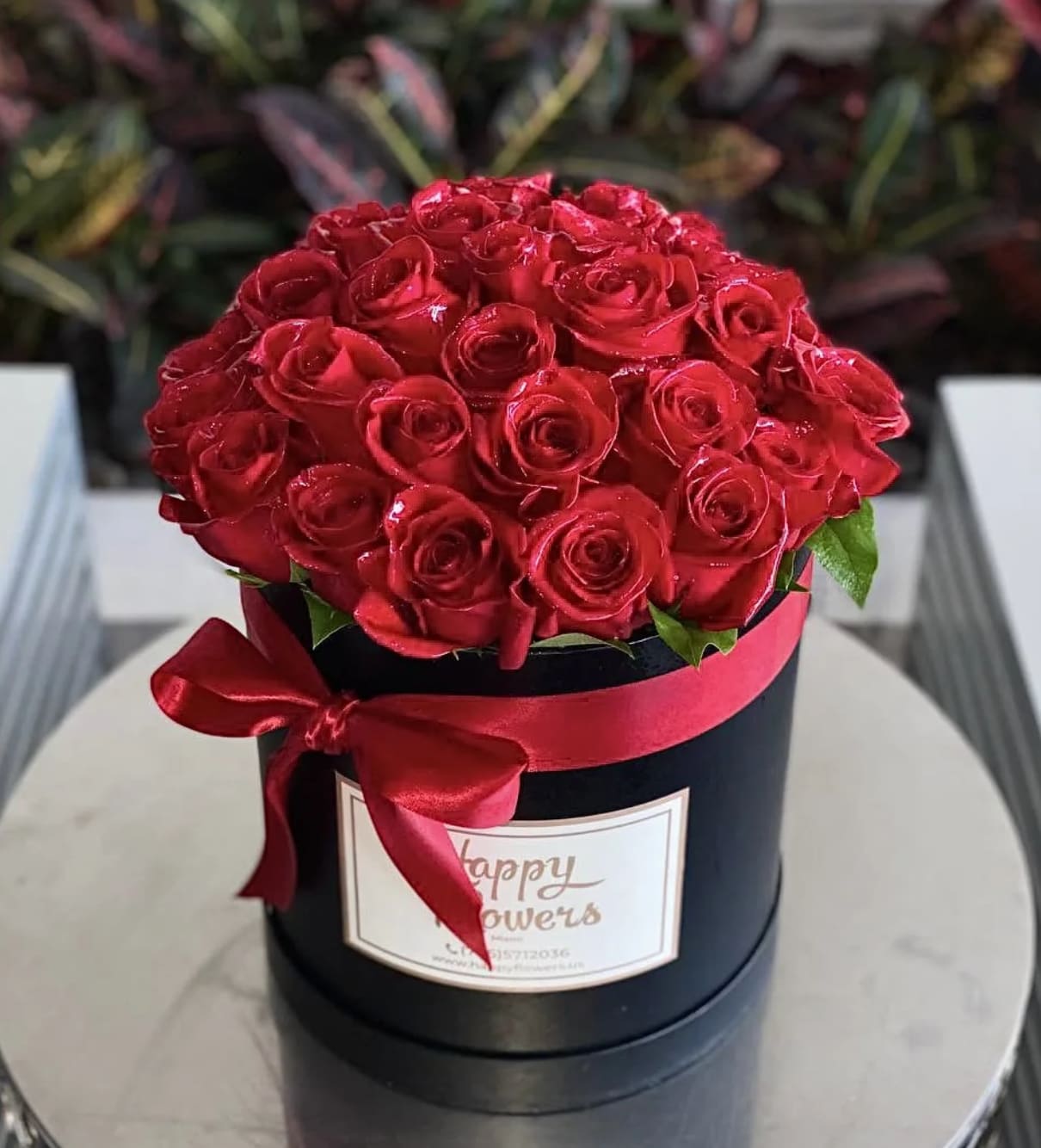 Red roses arranged in a black round box with a red ribbon