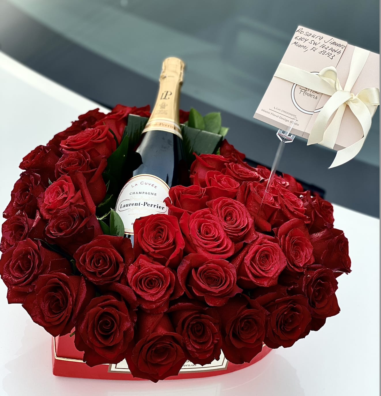 Red rose arrangement surrounding a champagne bottle in a gift box