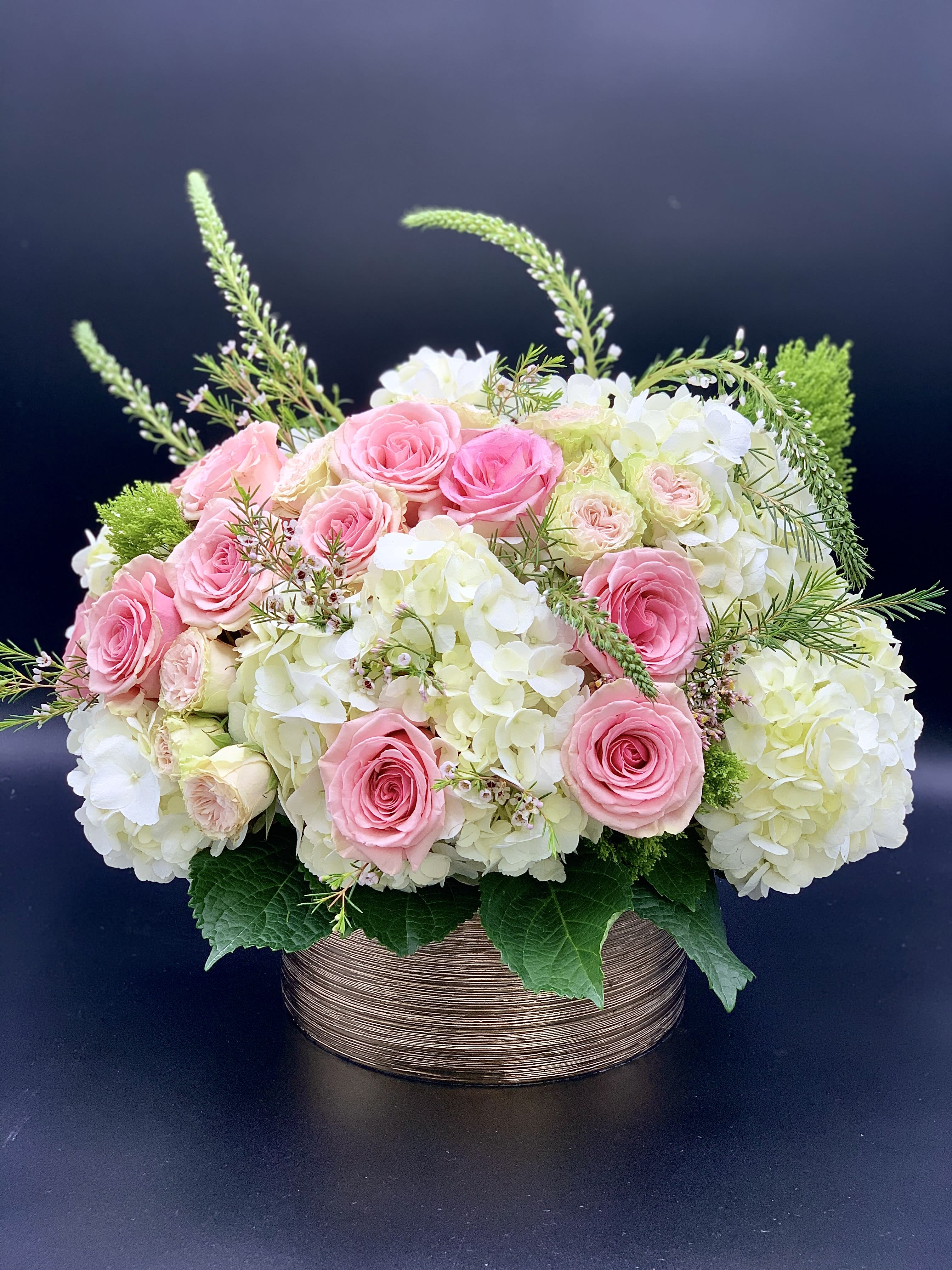 Pink roses and white hydrangeas in a round basket arrangement