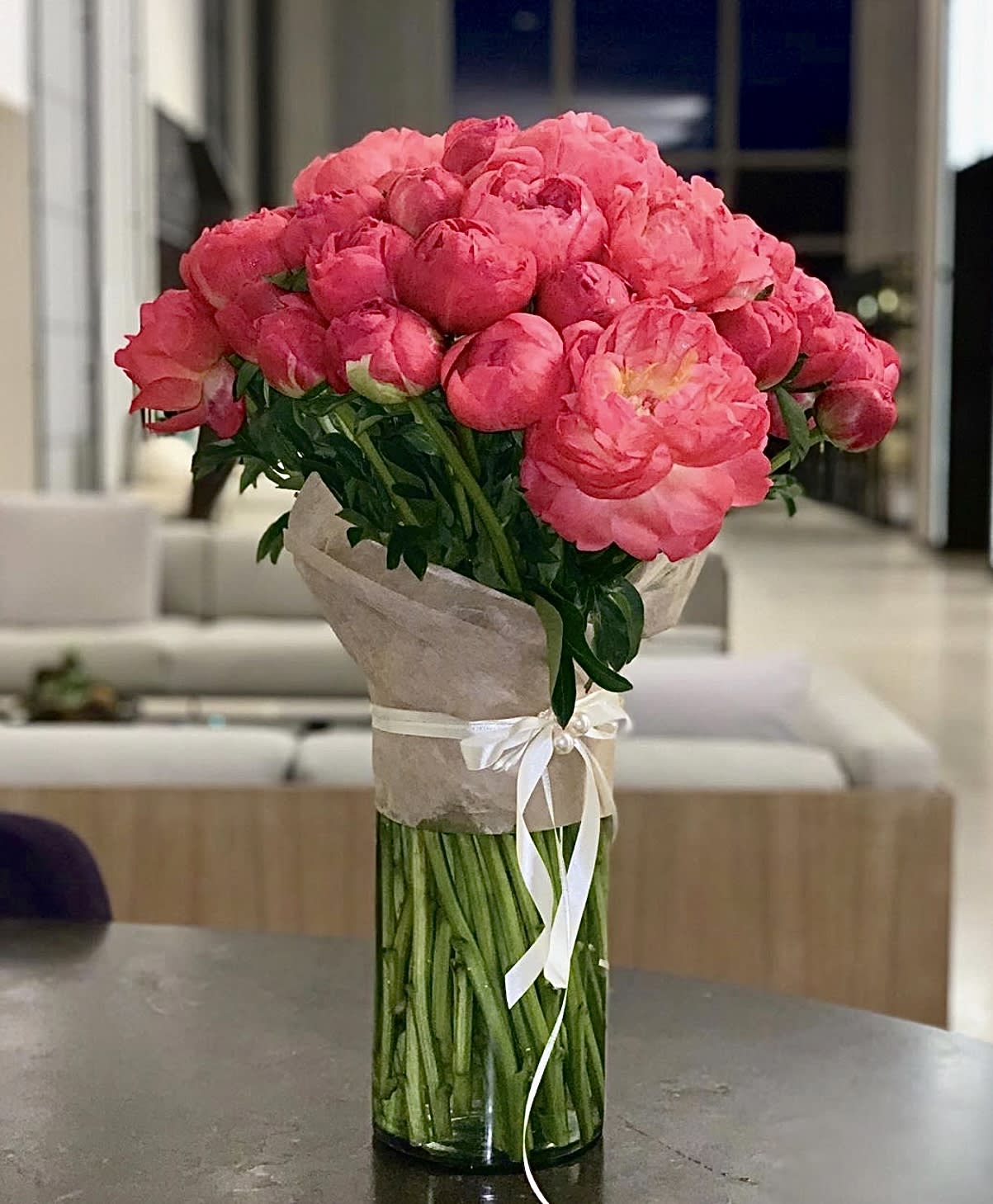 Bouquet of bright pink peonies in a tall glass vase with a ribbon wrap