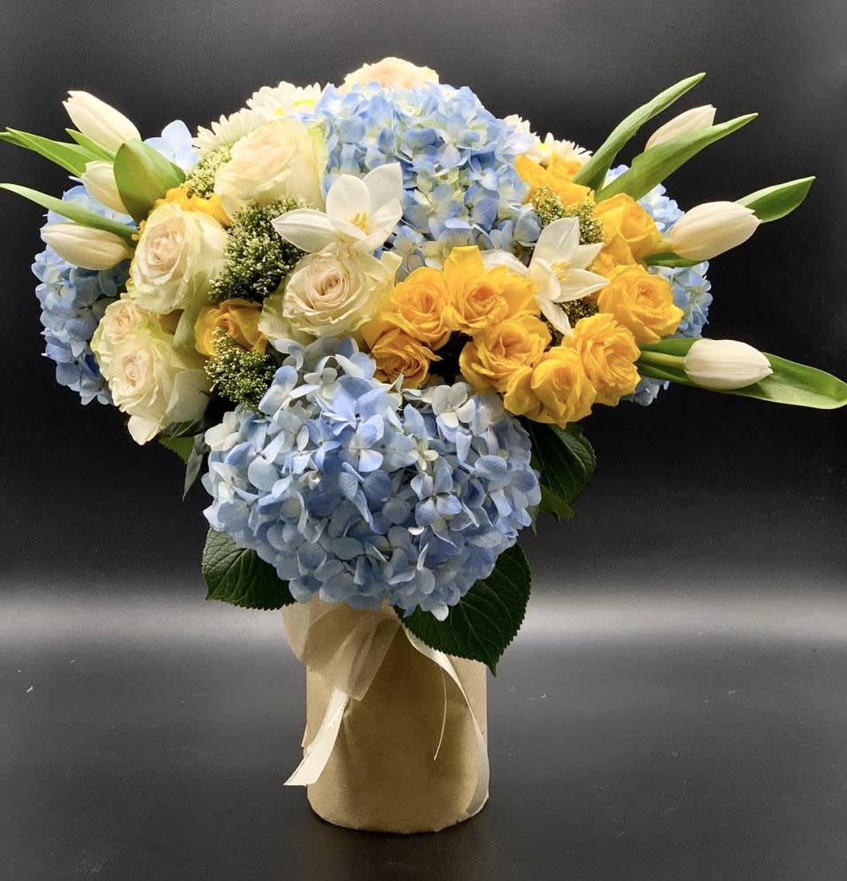 Blue hydrangeas with yellow and white roses in a wrapped vase arrangement