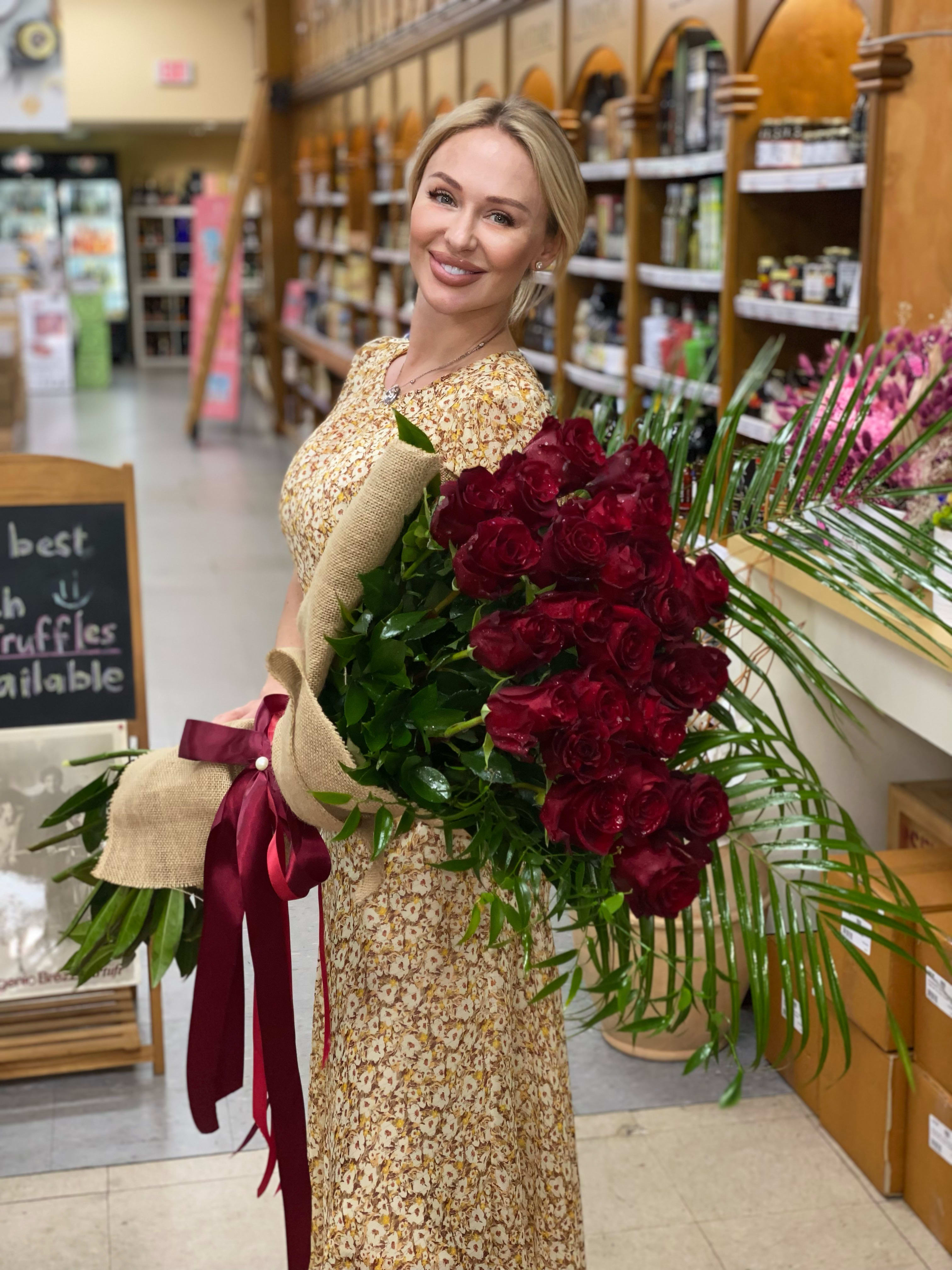 Woman holding a large bouquet of red roses wrapped in burlap with a burgundy ribbon