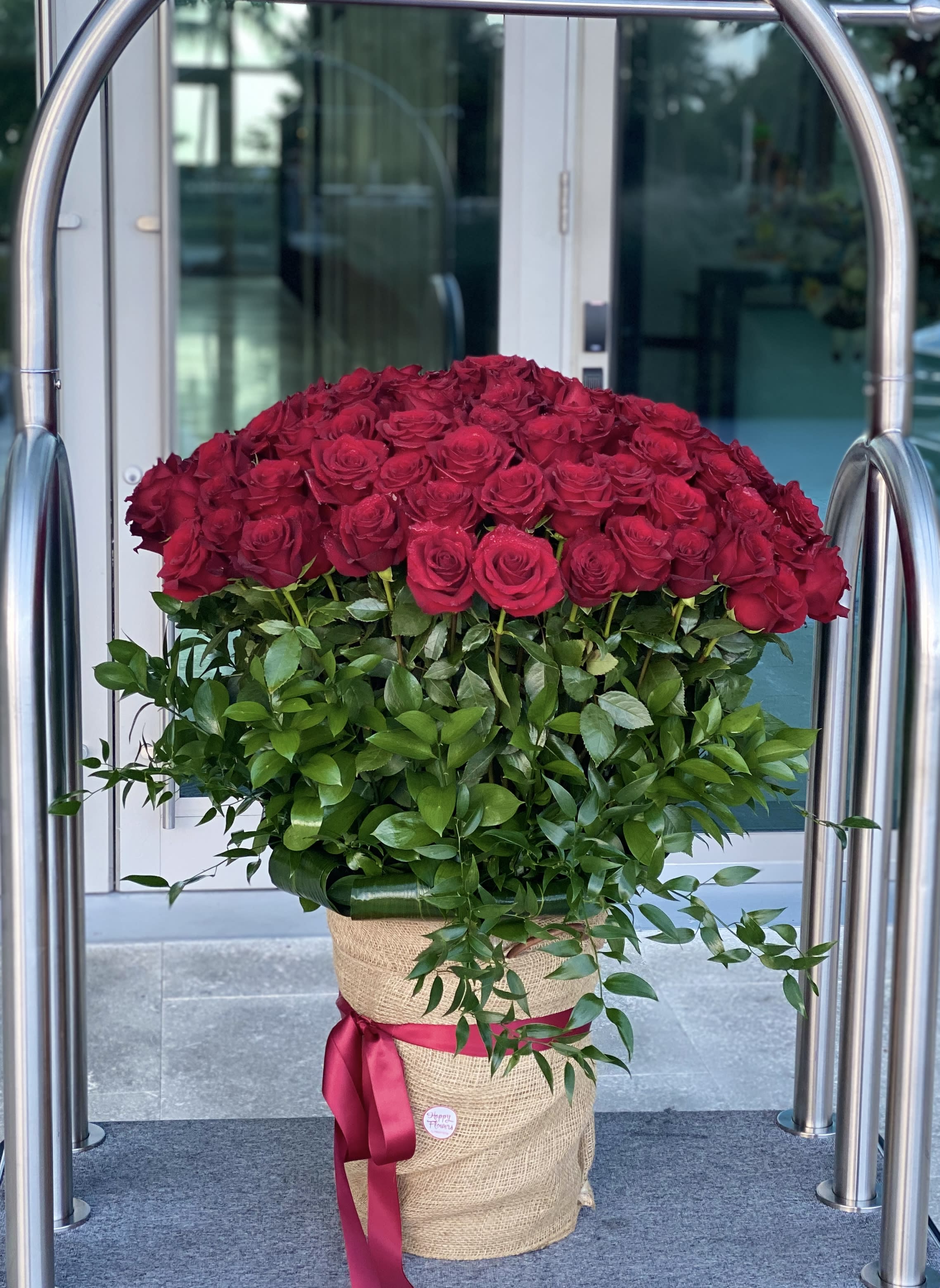 Large bouquet of red roses in a burlap-wrapped container with a pink ribbon