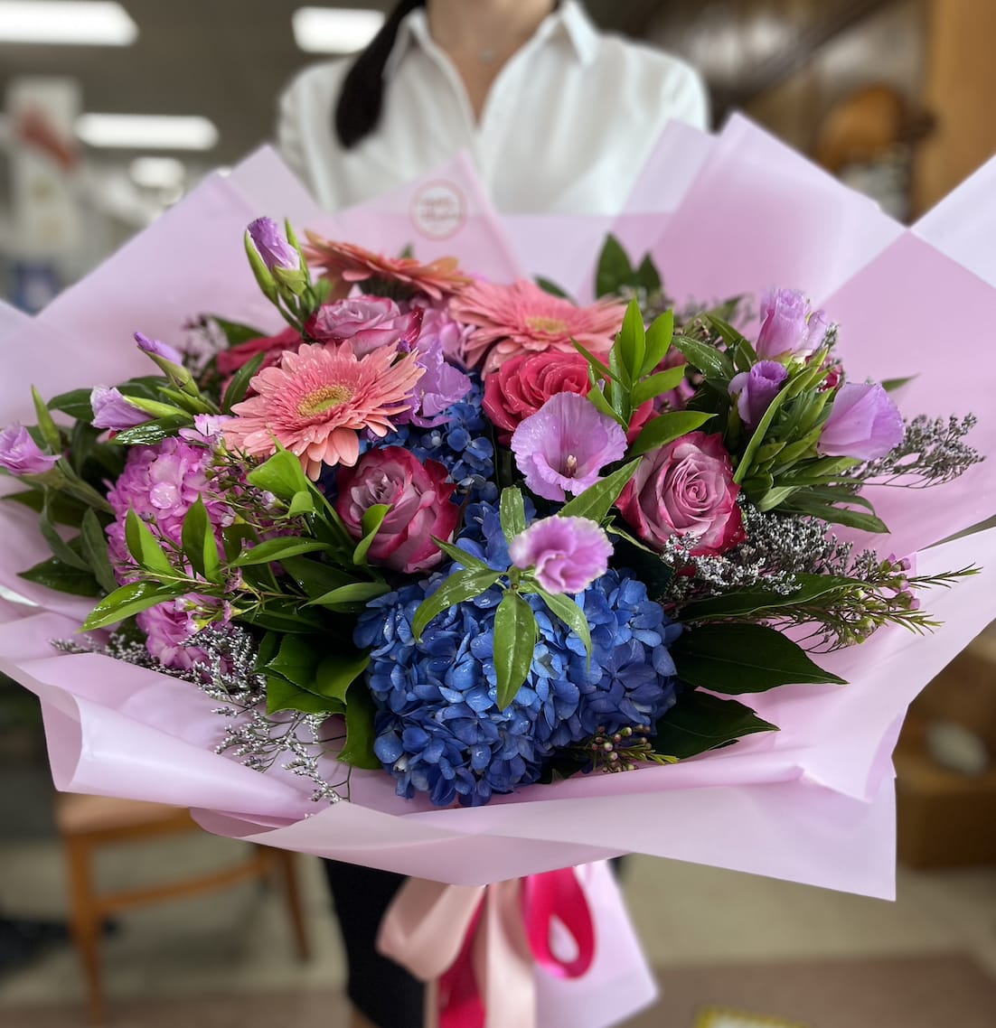 Bouquet of pink and purple flowers with blue hydrangeas wrapped in pink paper