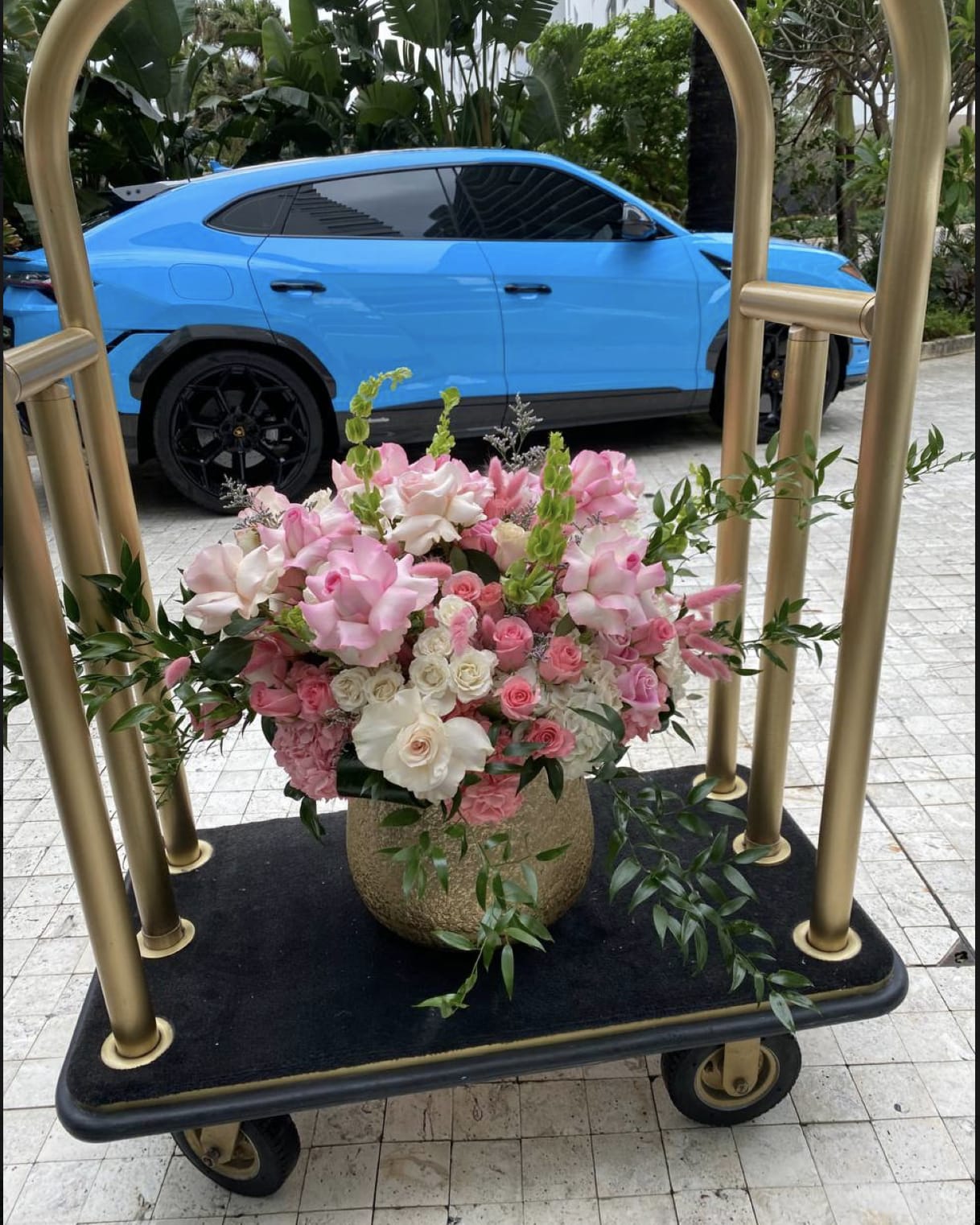 Pink and white floral arrangement in a gold vase on a cart