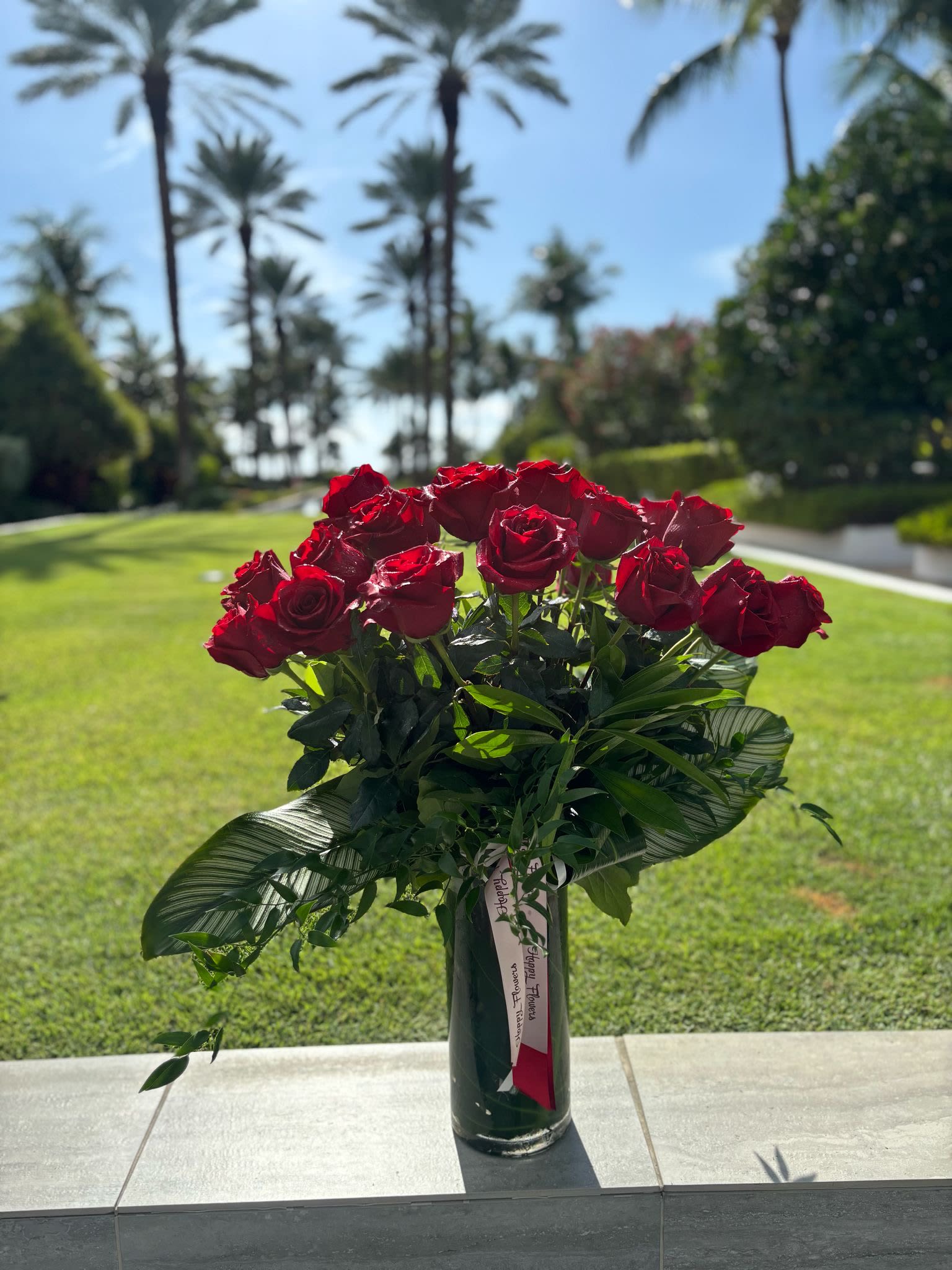 Red roses arranged in a tall glass vase outdoors
