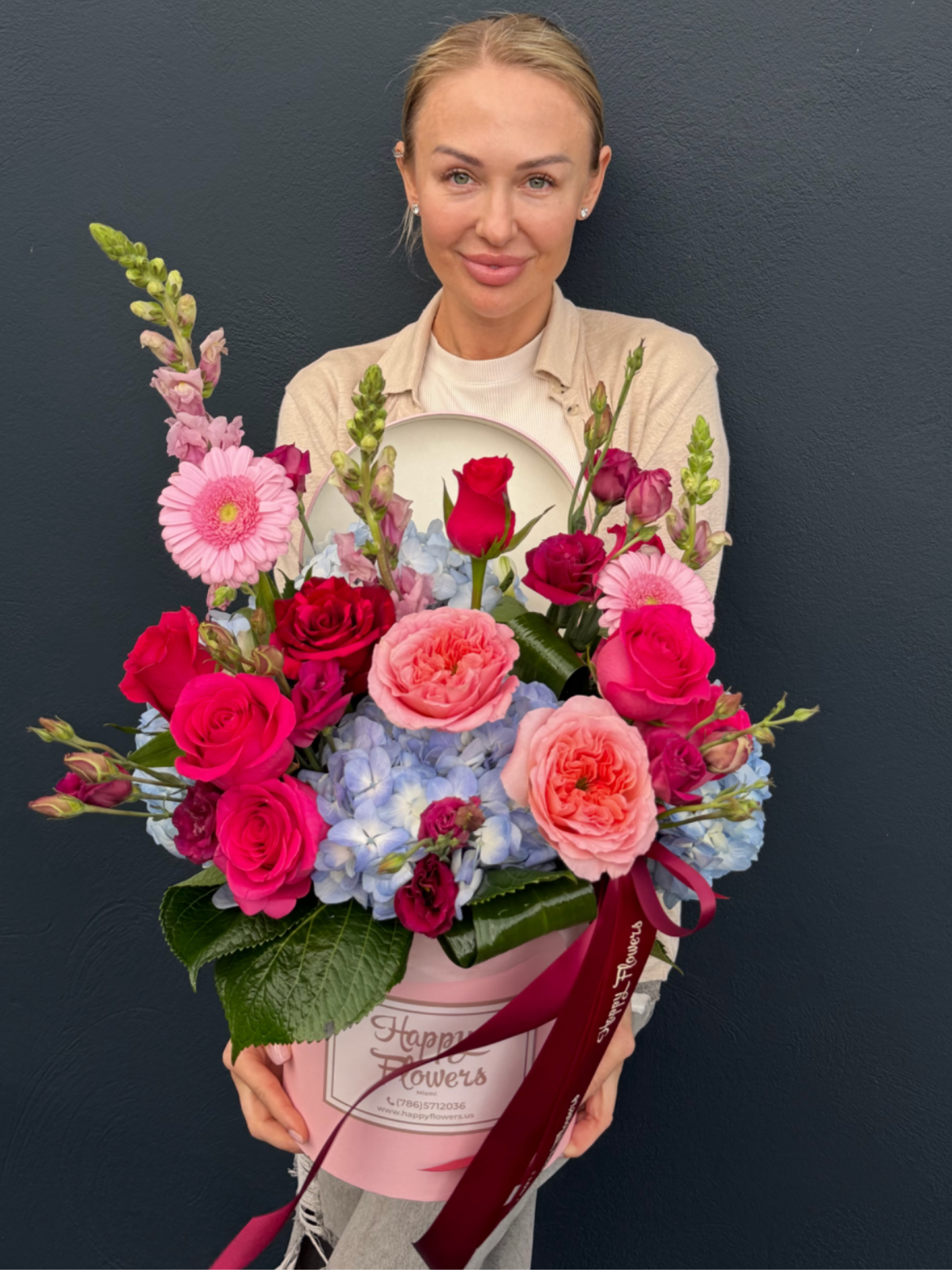 Bright day  - A lush hatbox of hot pink and red roses layered over pale blue hydrangeas creates an immediate lift-this flower arrangement is a bright, romantic gift perfect for birthdays, anniversaries, or Valentine's Day. Tall pink snapdragon spikes give the design elegant height while blush garden roses and pink gerbera daisies soften the center, so the person you're celebrating will feel truly noticed and adored from first glance.  Carefully arranged in a pink round hatbox with a satin and decorative ribbon and a matching lid, the presentation reads like a polished gift the moment it arrives. The large, rounded silhouette is tightly packed for a full, luxurious look; colors range from saturated hot pinks and reds to soft peaches, blushes, pale blue, white and lavender tones for depth. For best enjoyment, keep the box in a cool spot away from direct sun and replace water per the included care insert so blooms stay fresh longer.