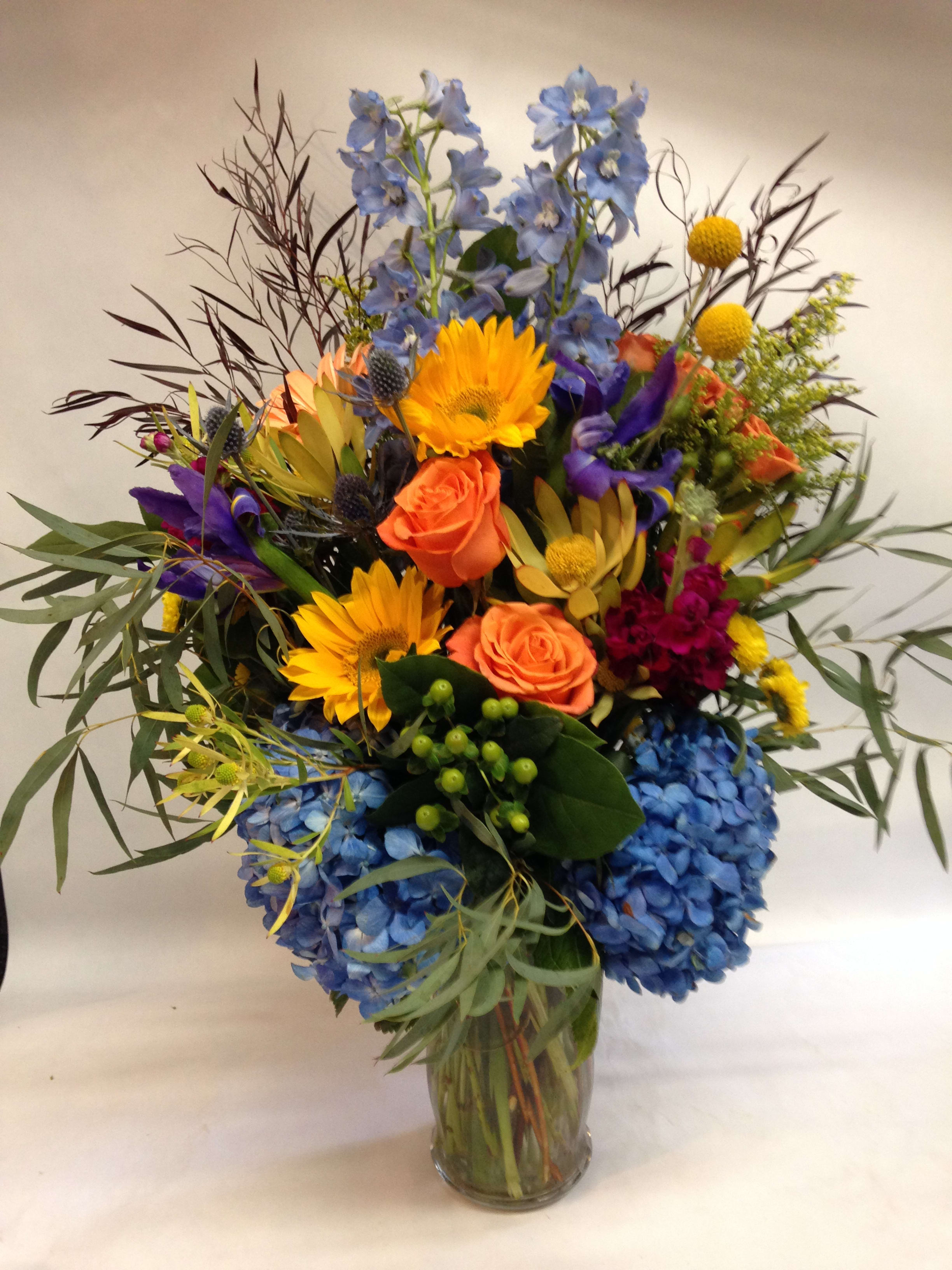 Colorful mixed bouquet in a clear glass vase with blue hydrangeas and orange roses