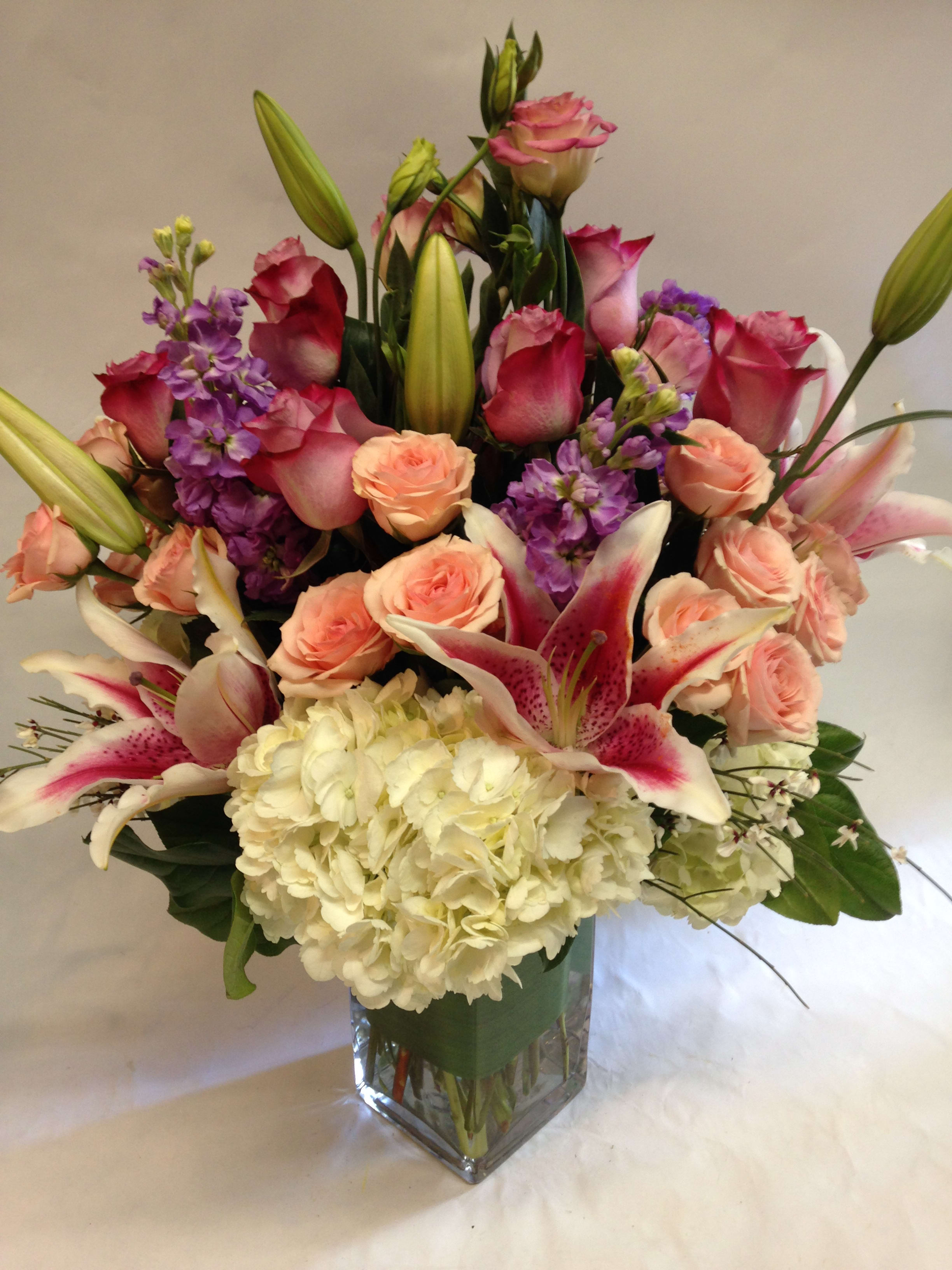 Mixed bouquet of pink roses, lilies, and white hydrangea in a glass vase
