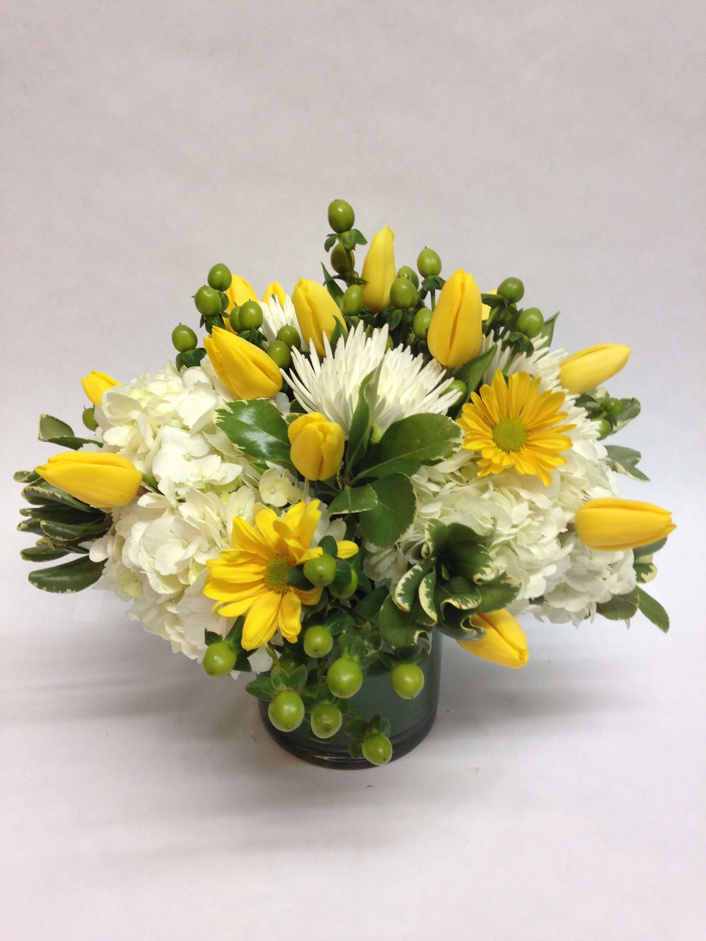 Yellow tulips and white flowers in a dark glass vase