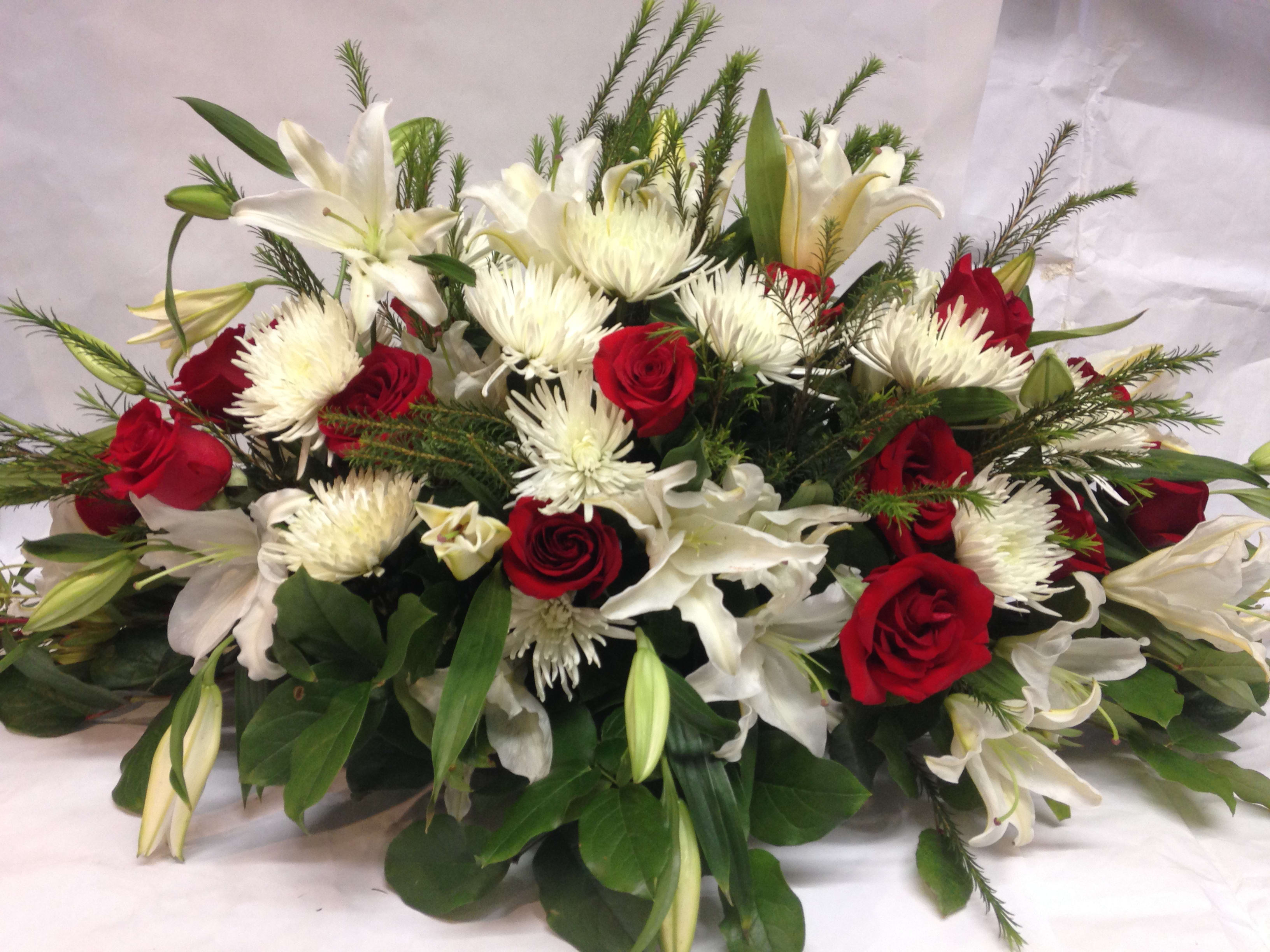 Red roses and white lilies arranged with white spider mums.