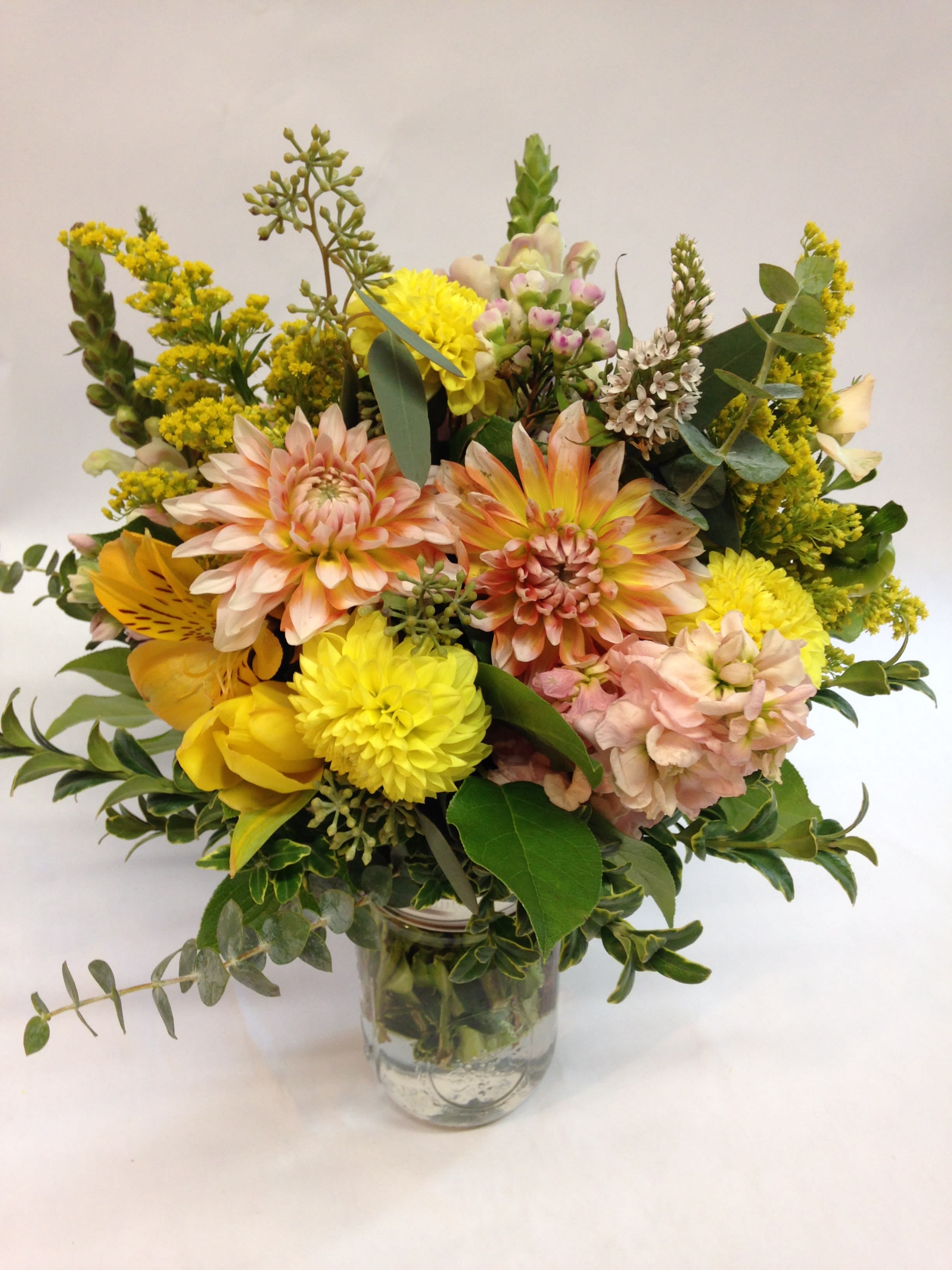 Mixed yellow and peach flowers arranged in a clear glass vase