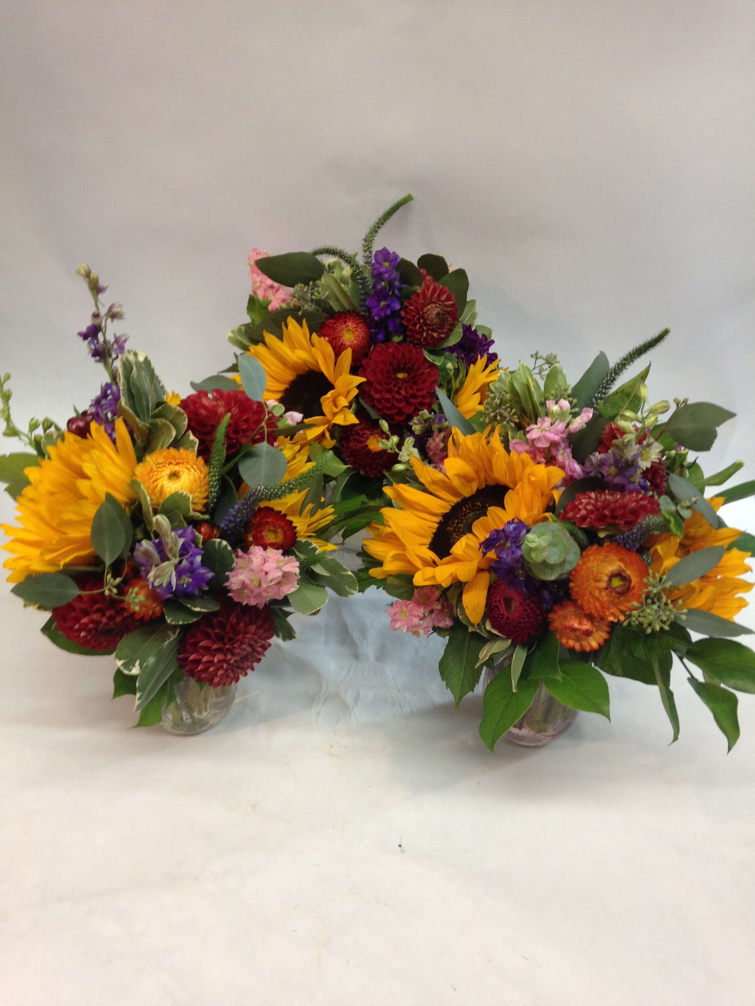 Three colorful flower arrangements in glass vases with sunflowers and mixed blooms