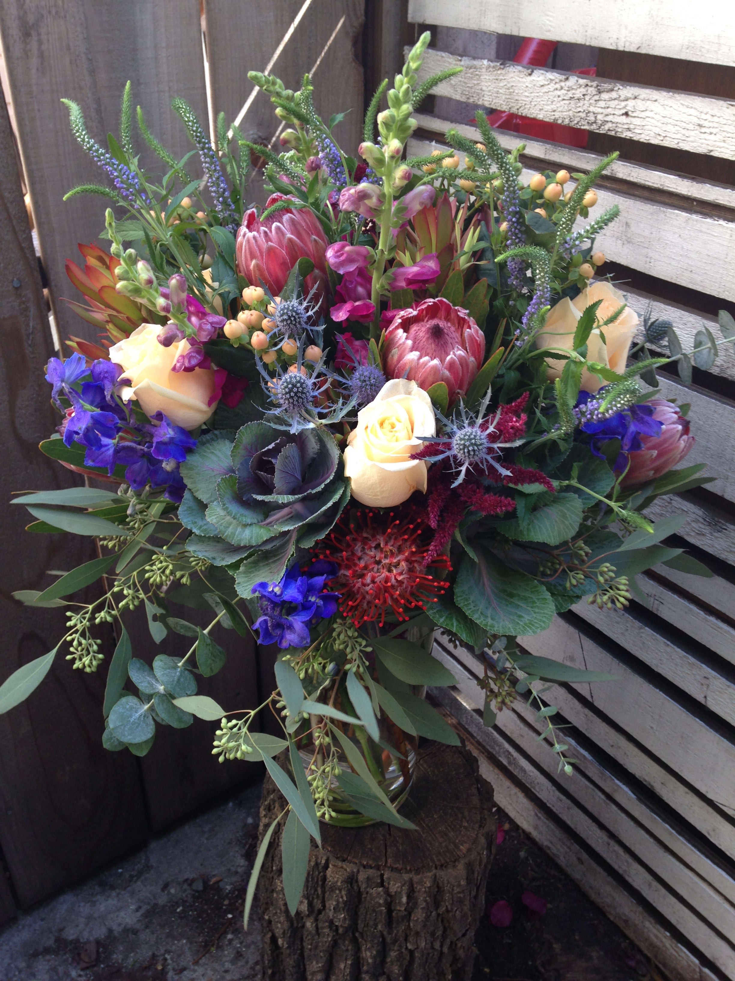 Mixed bouquet with protea, roses, and blue flowers in a glass vase