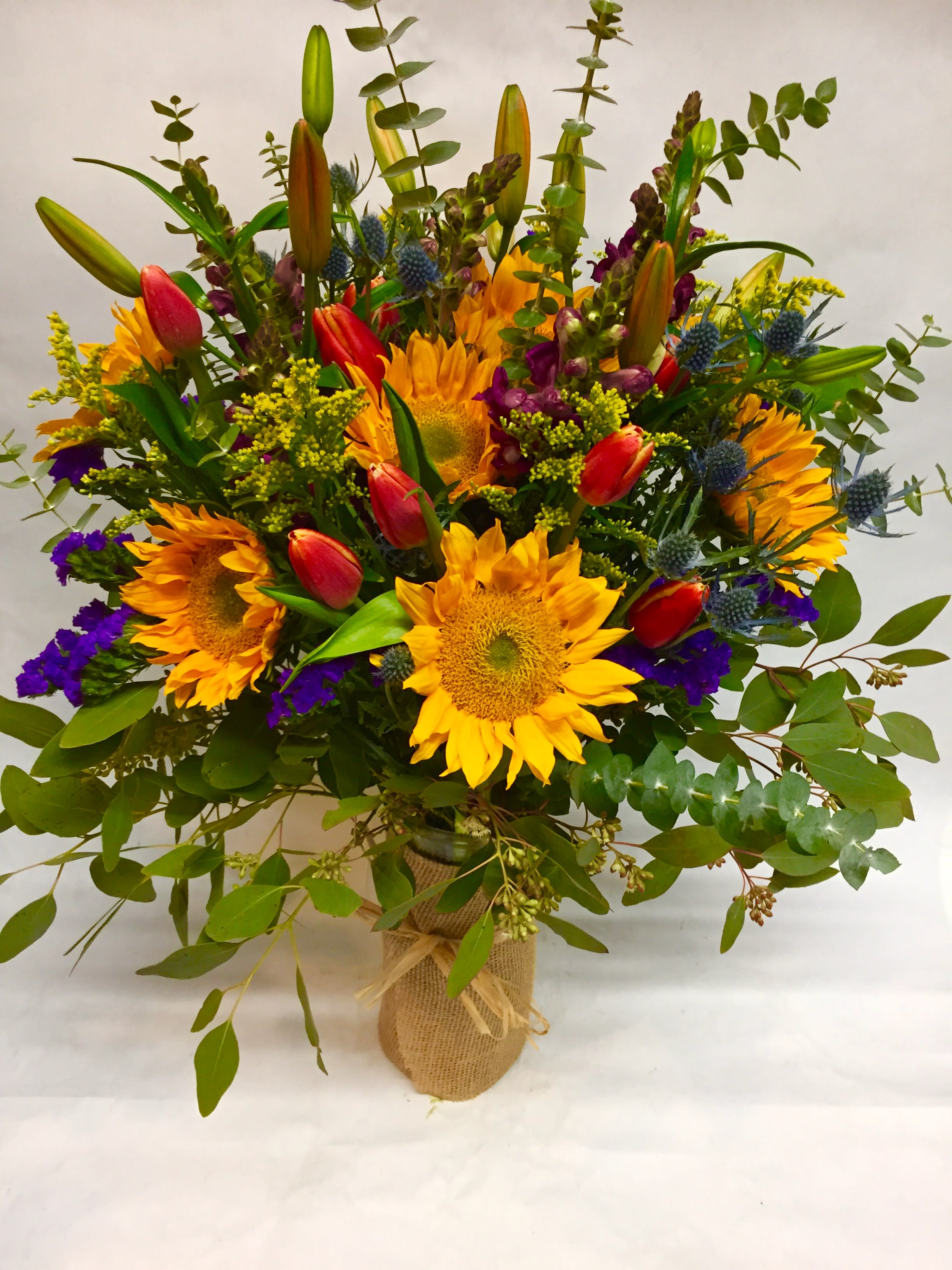 Bouquet of sunflowers, tulips, and purple accents in a burlap-wrapped vase