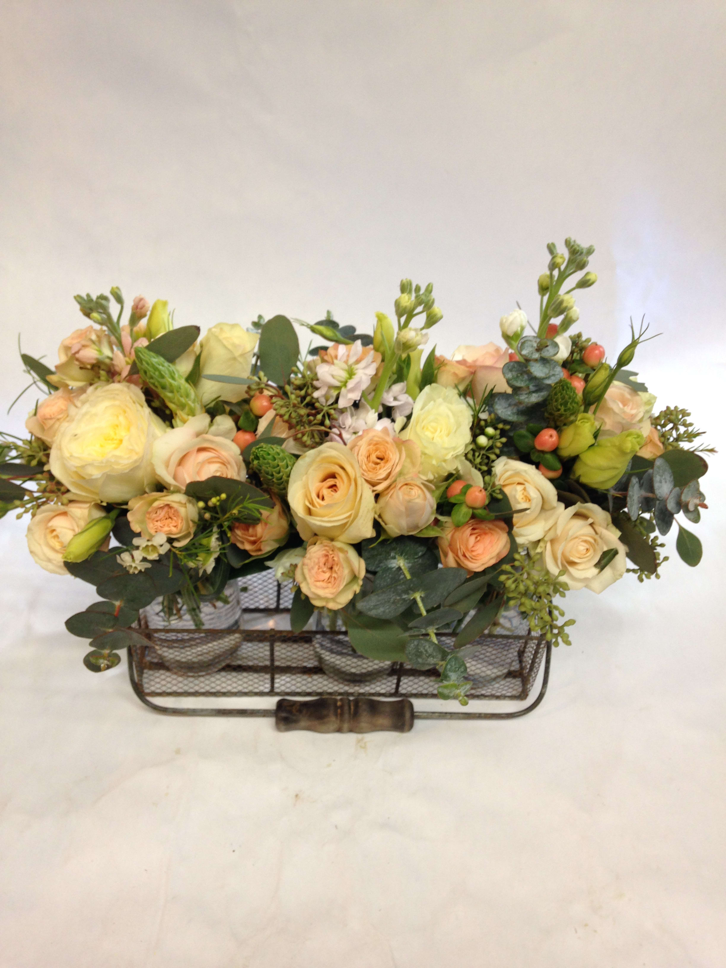 Low floral arrangement of cream and peach roses in a metal basket