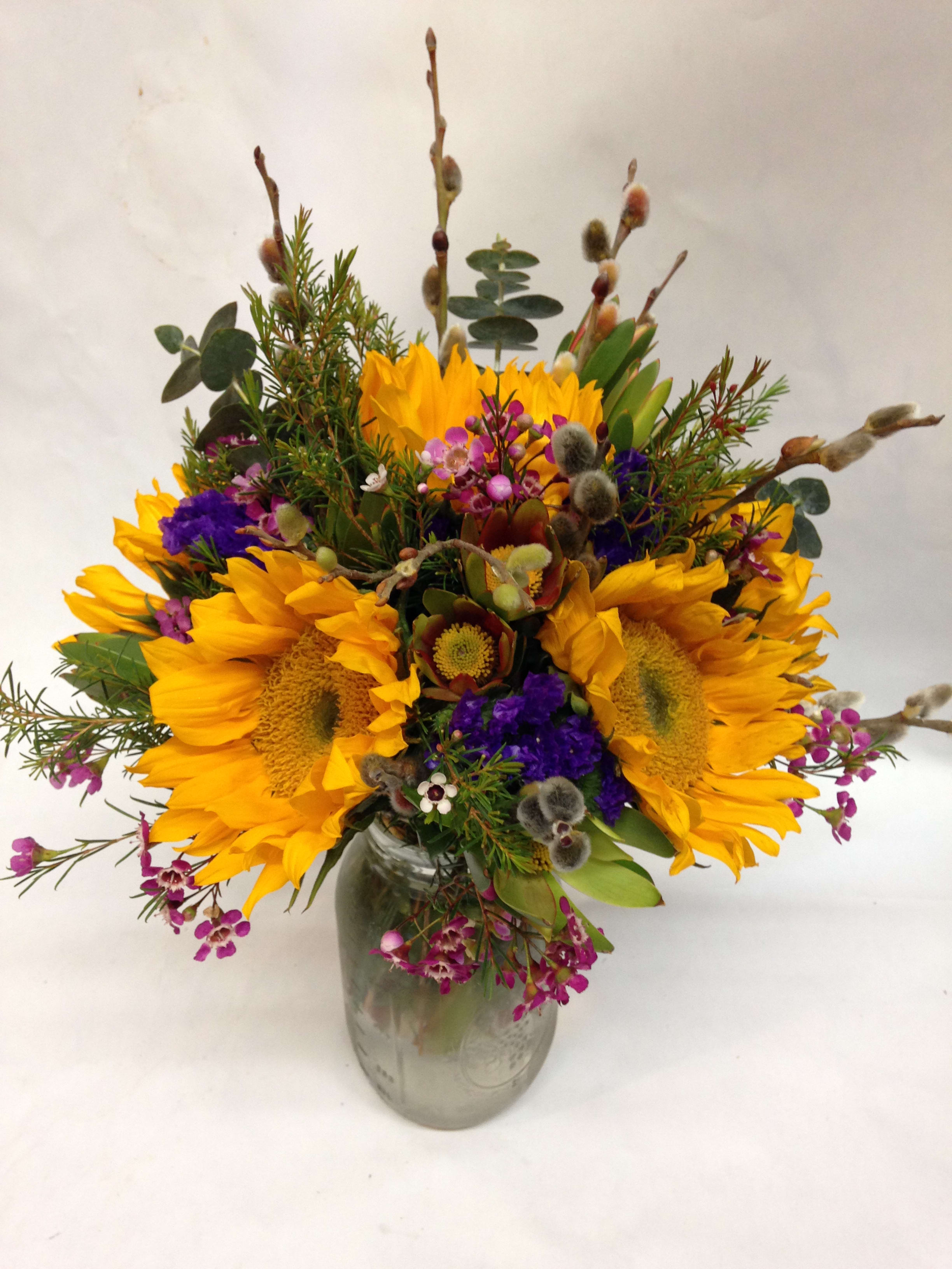 Mason jar arrangement of yellow sunflowers with purple and pink accent flowers