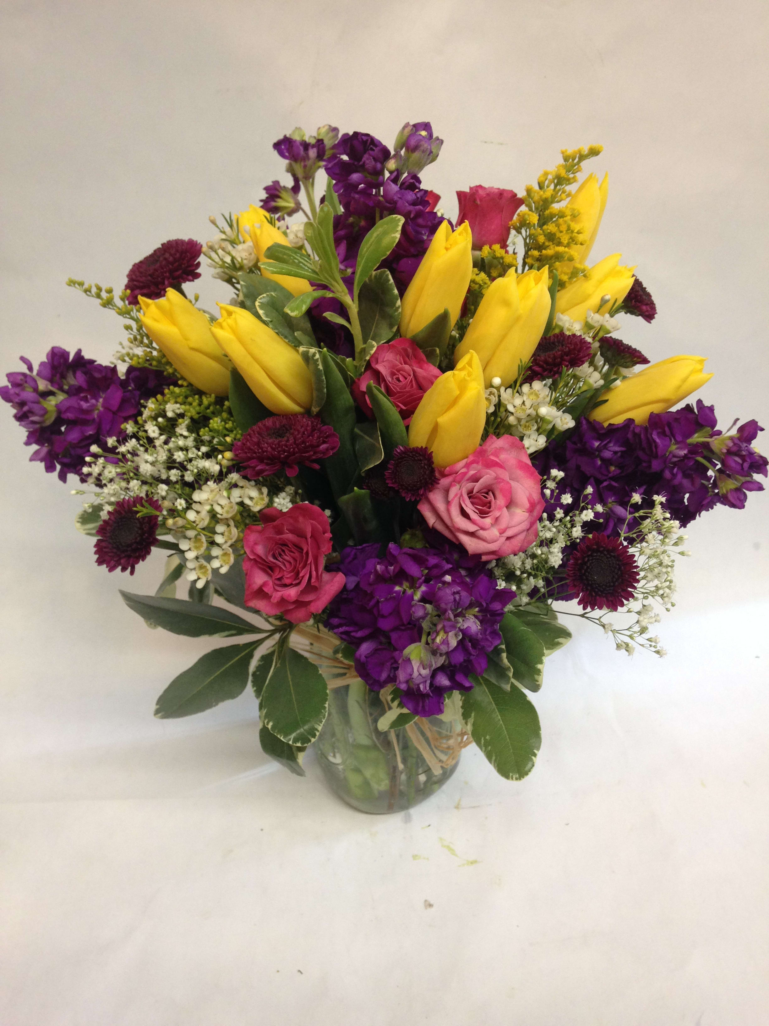 Bouquet of yellow tulips, pink roses, and purple flowers in a glass vase