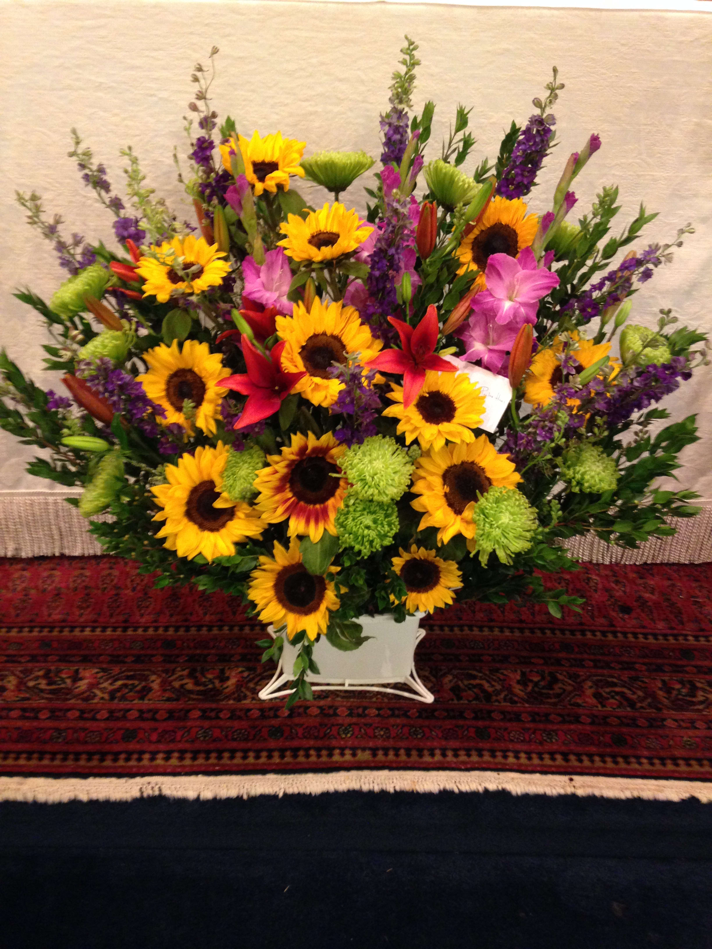 Large mixed bouquet with sunflowers, lilies, and purple flowers in a white container