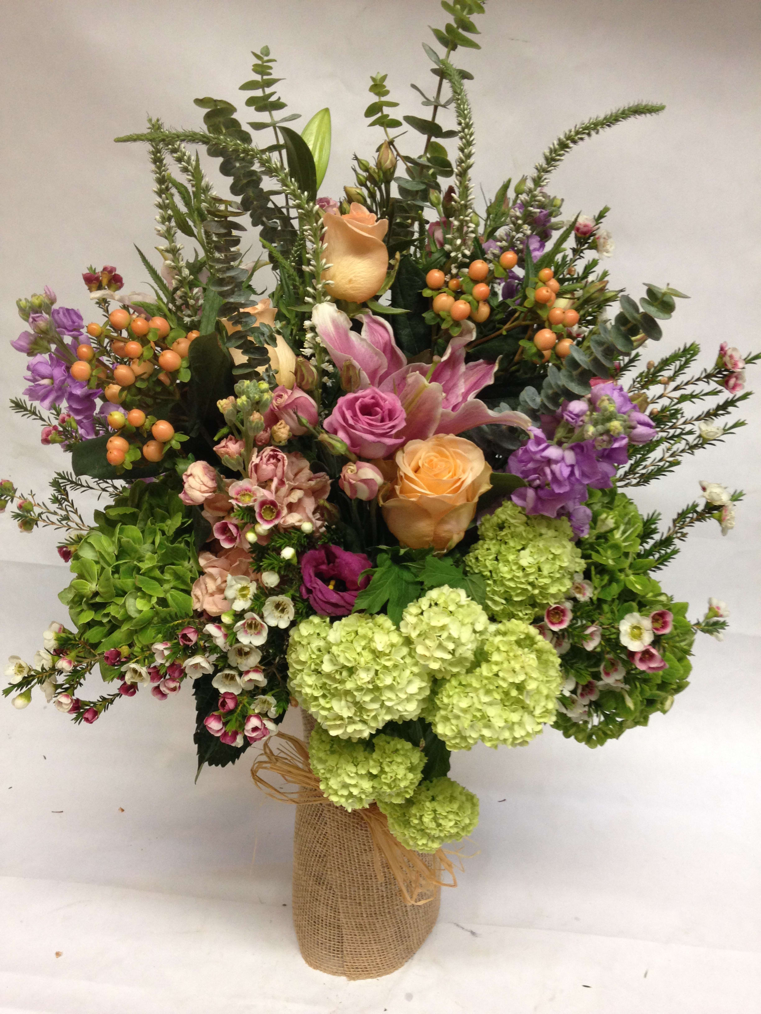 Mixed bouquet with roses, lilies, hydrangeas, and berries in a burlap-wrapped vase
