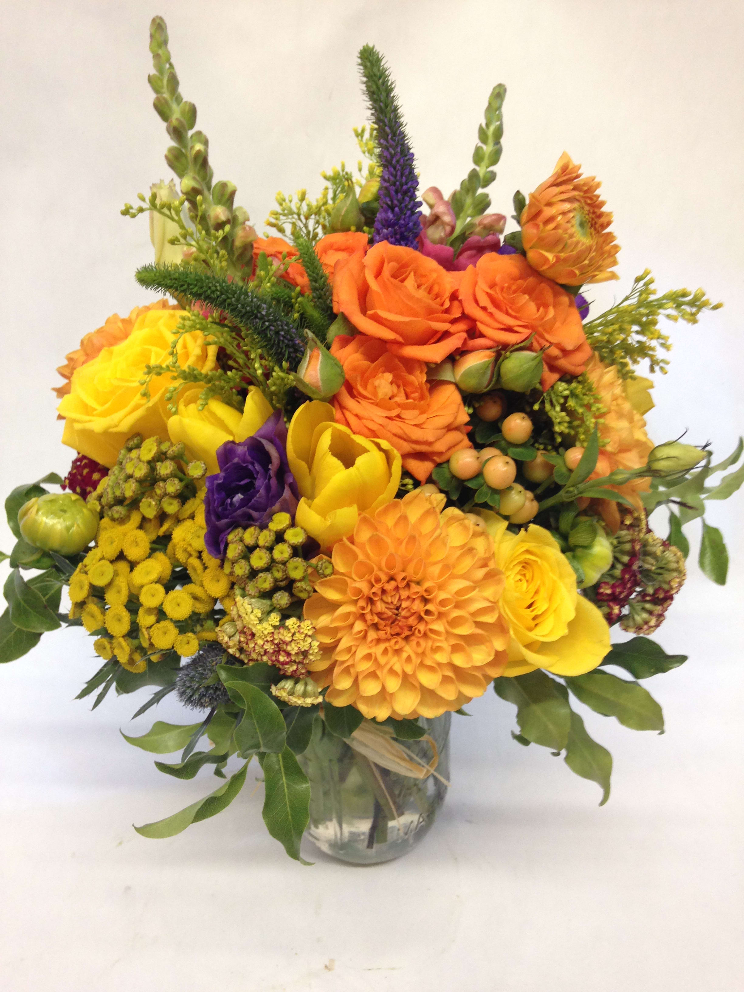 Bright mixed bouquet of orange, yellow, and purple flowers in a glass vase
