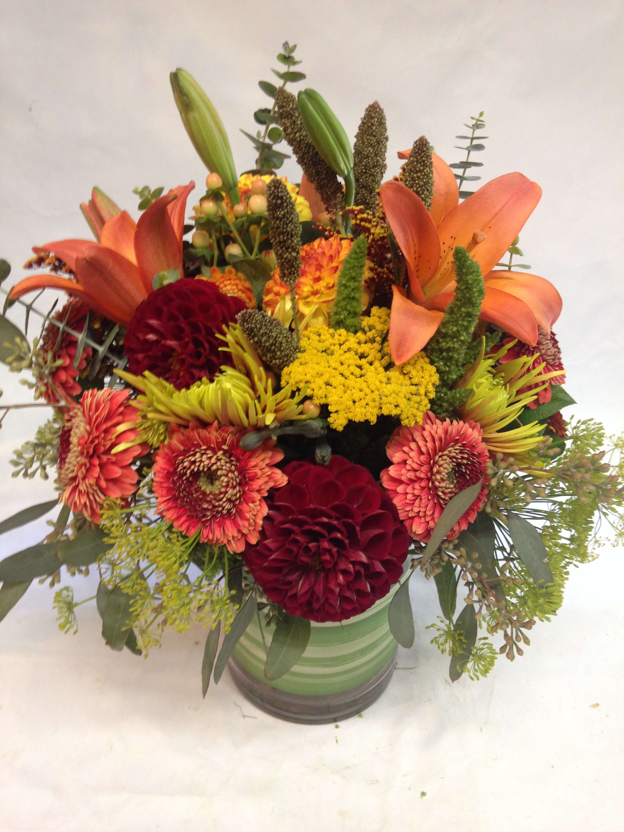 Feeling like Fall - This gorgeous centerpiece is dripping with seasonal charm! Featuring orange lilies, burgundy flowers , yarrow, and seasonal greenery. (Some flowers may be subject to change depending on the season. We will contact you with available flower substitutions; please contact us with specific questions if you are concerned with flower availability, thanks!)  Featured Arrangement: $145.00