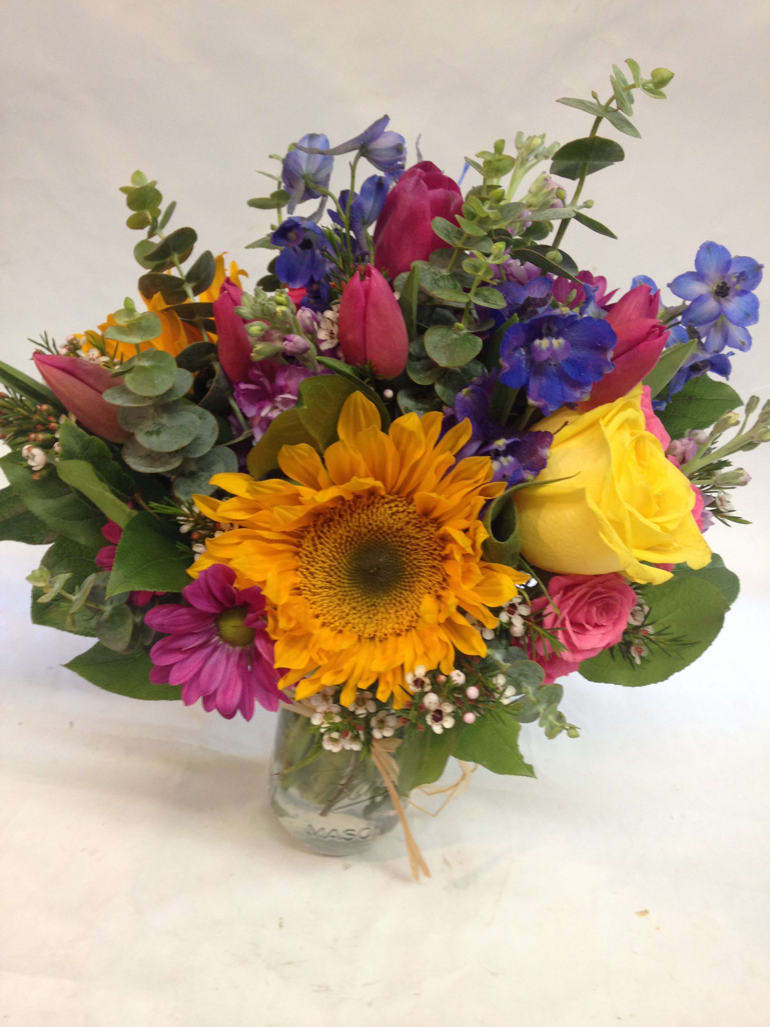 Mixed bouquet with sunflowers, roses, and blue flowers in a glass vase