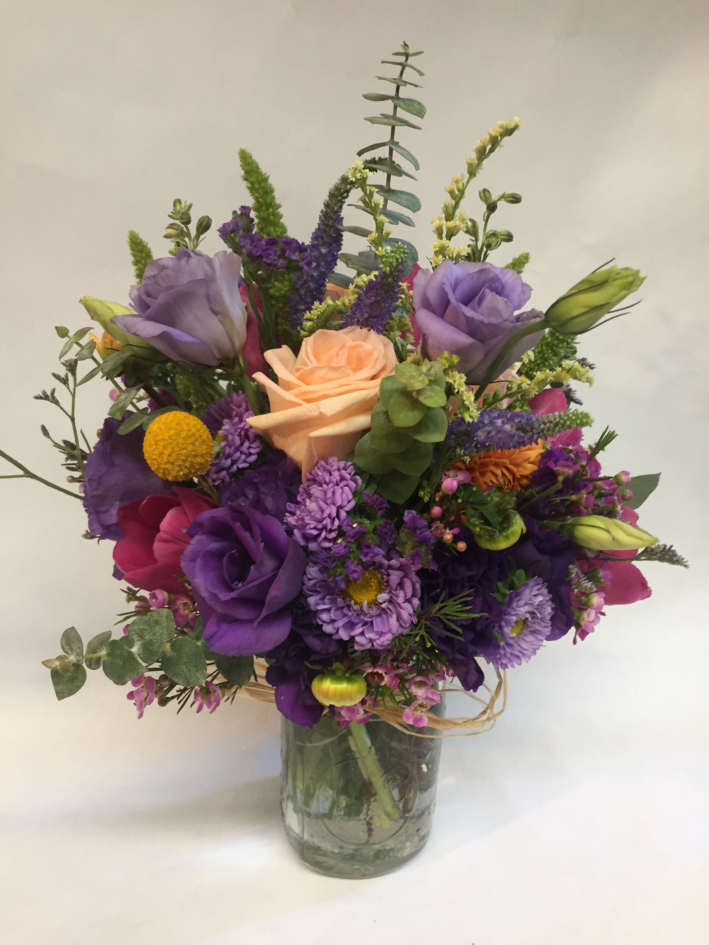 Mixed bouquet of purple, peach, and pink flowers in a glass vase