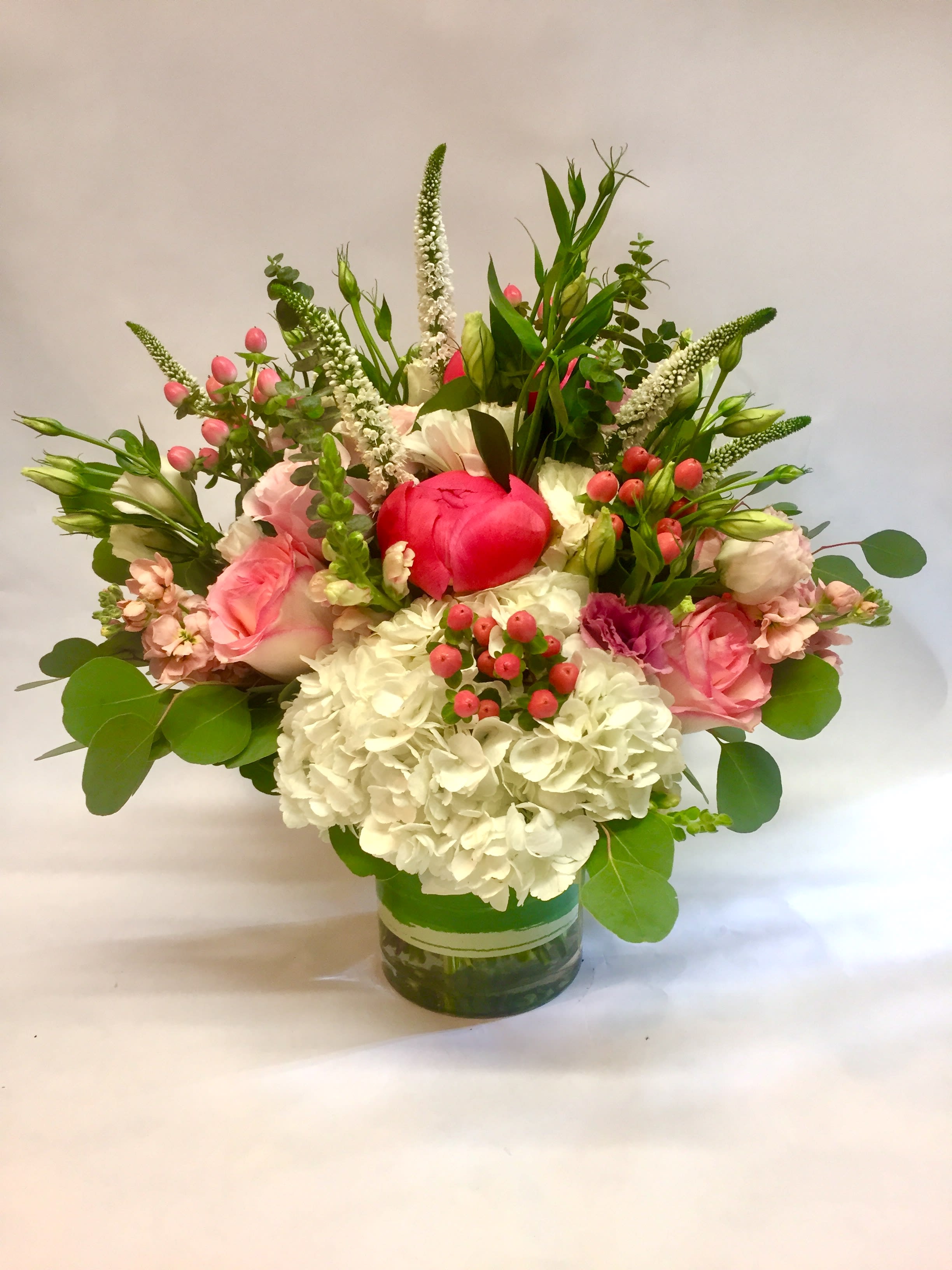 Pink and white flower arrangement with hydrangeas and roses in a clear glass cylinder vase