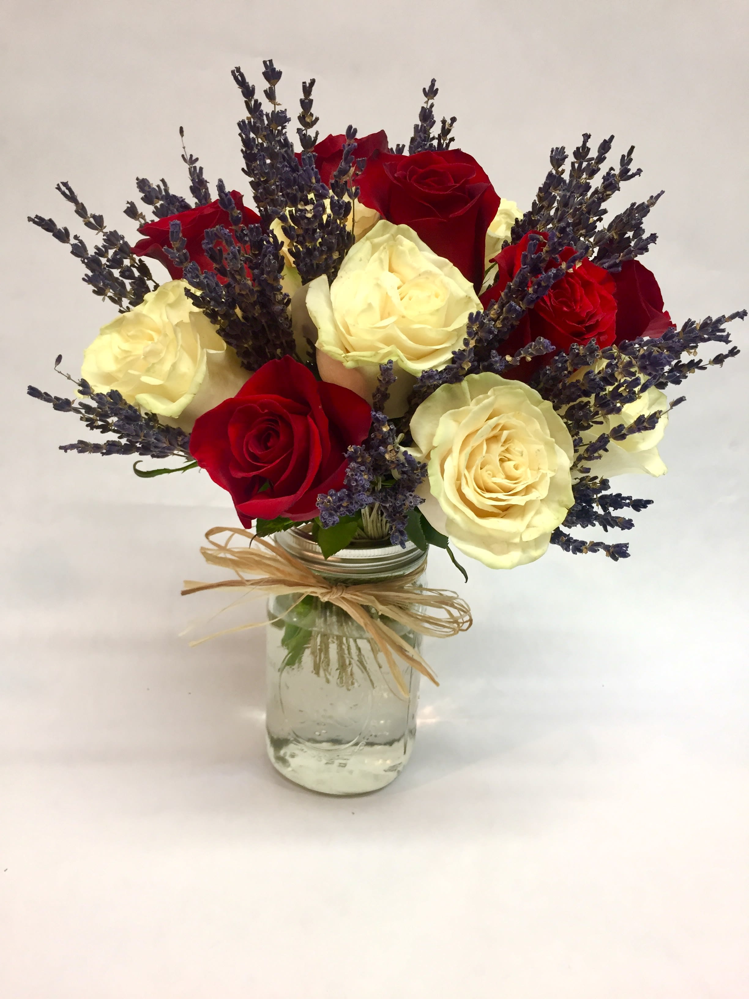 Red and cream roses with purple lavender in a glass jar vase