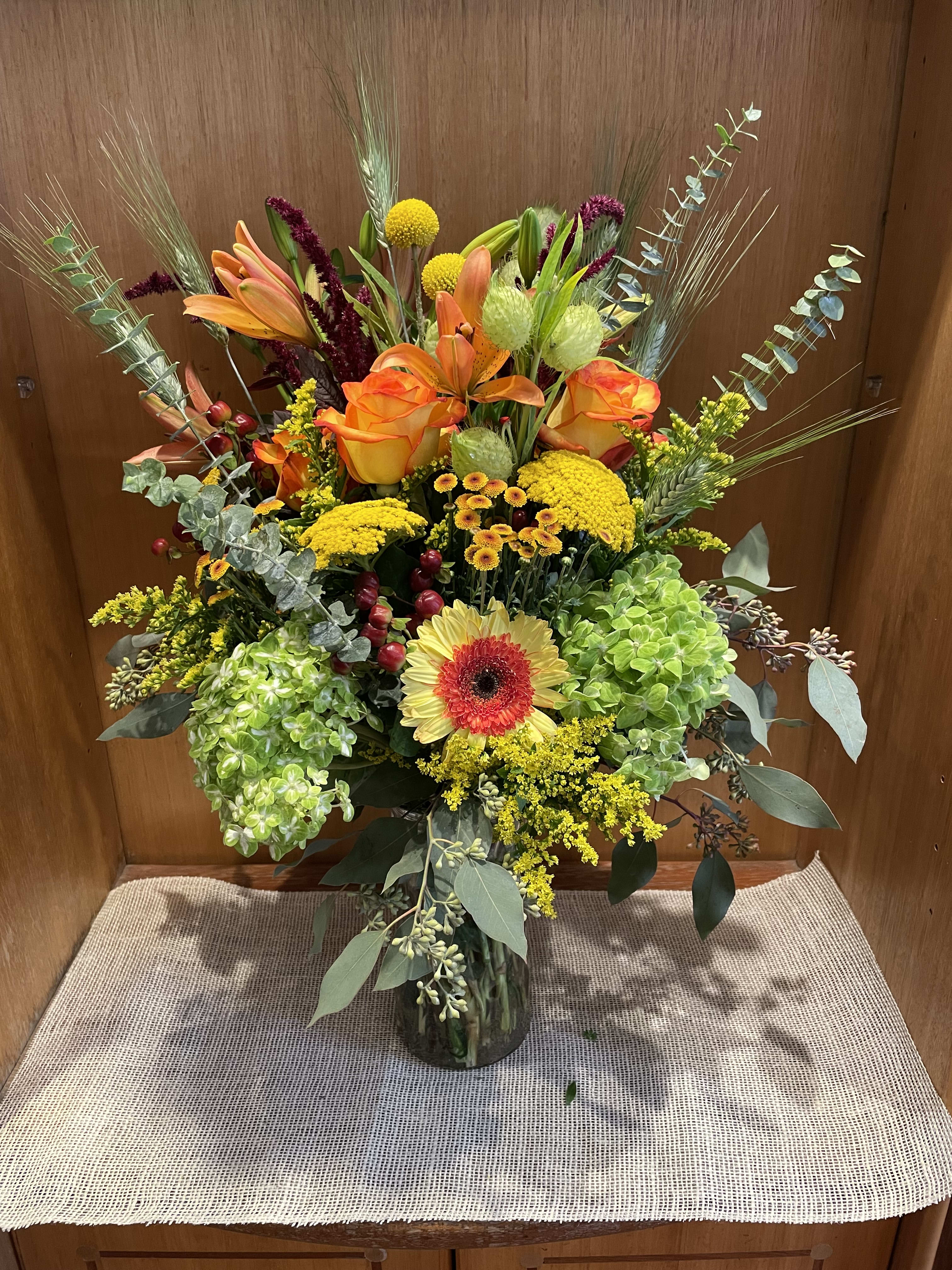 Tall mixed bouquet in a glass vase with orange roses and lilies