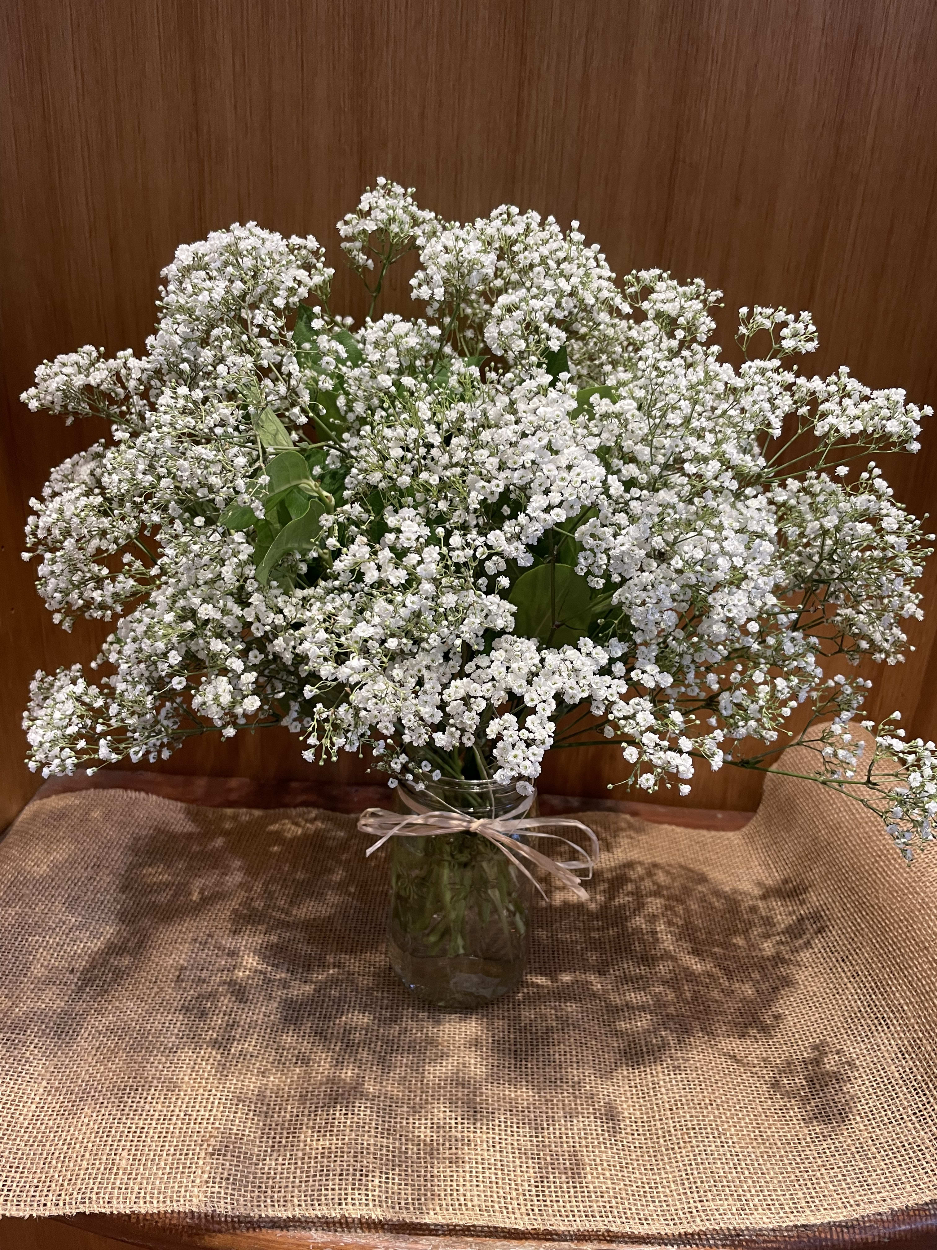 White baby's breath bouquet in a glass vase with a ribbon