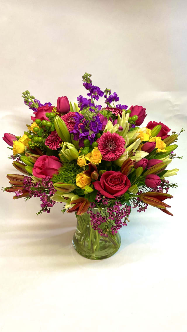 Mixed bouquet of pink, purple, and yellow flowers in a glass vase
