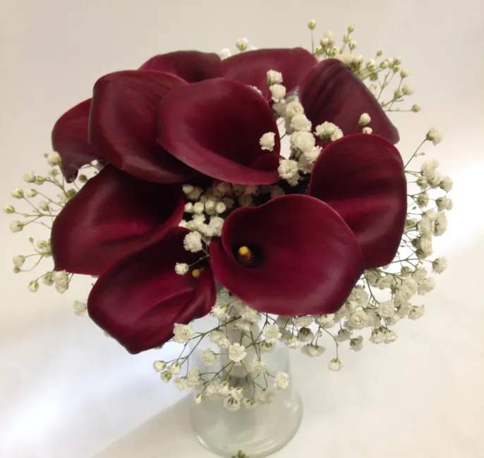 Deep burgundy calla lilies in a clear glass vase with white baby's breath