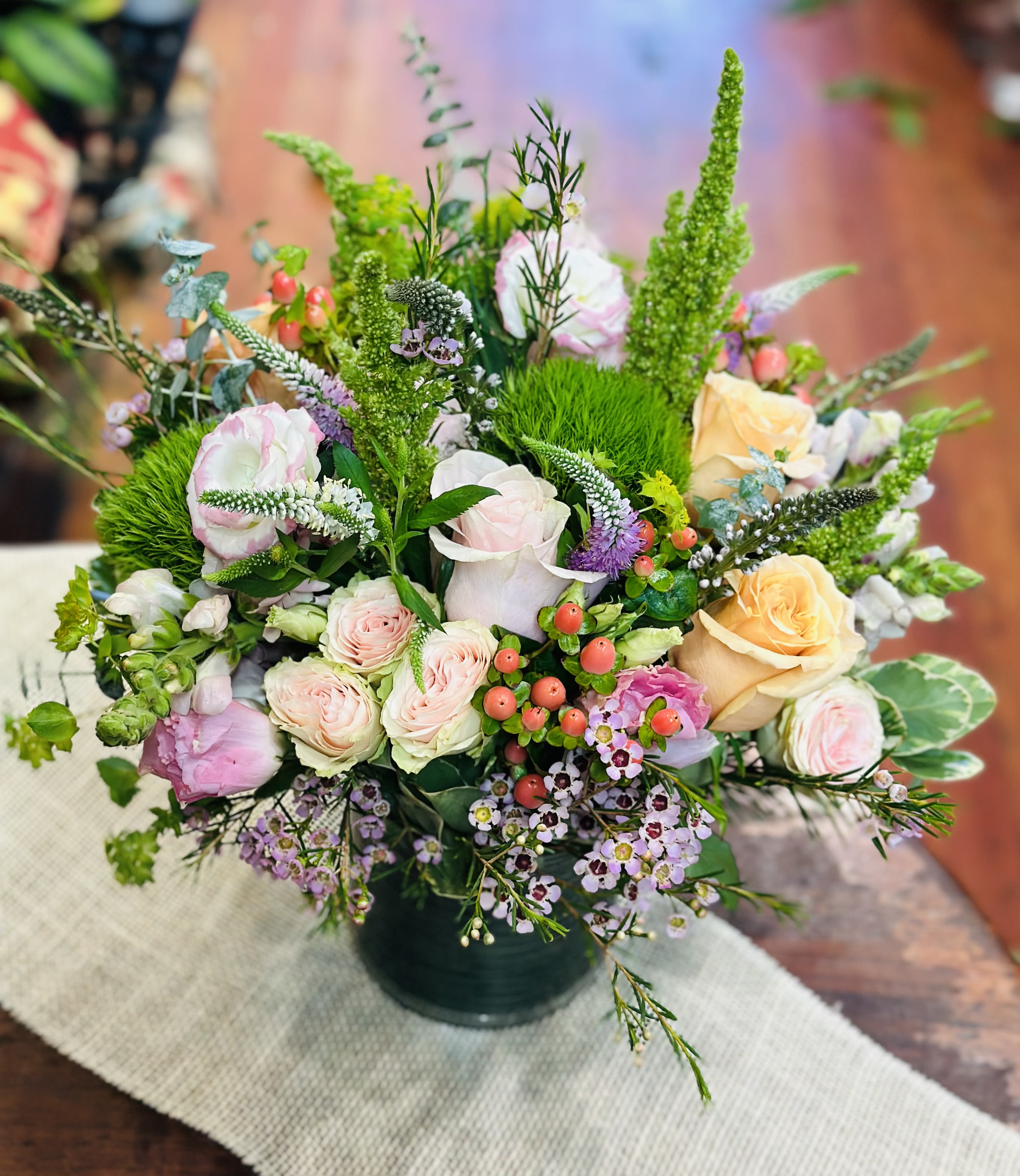 Mixed bouquet of pastel roses and small purple flowers in a dark vase