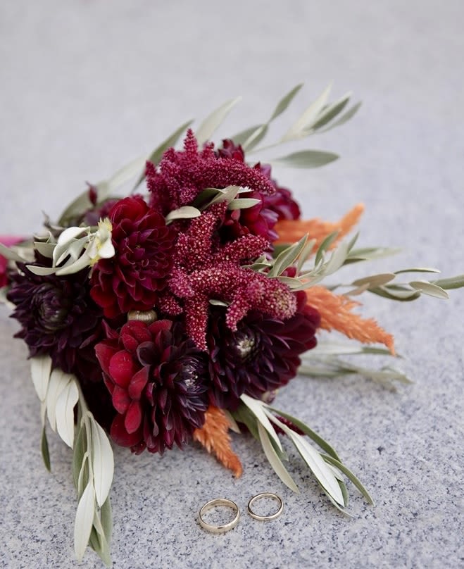 Deep red bouquet with orange accents and two rings on a stone surface