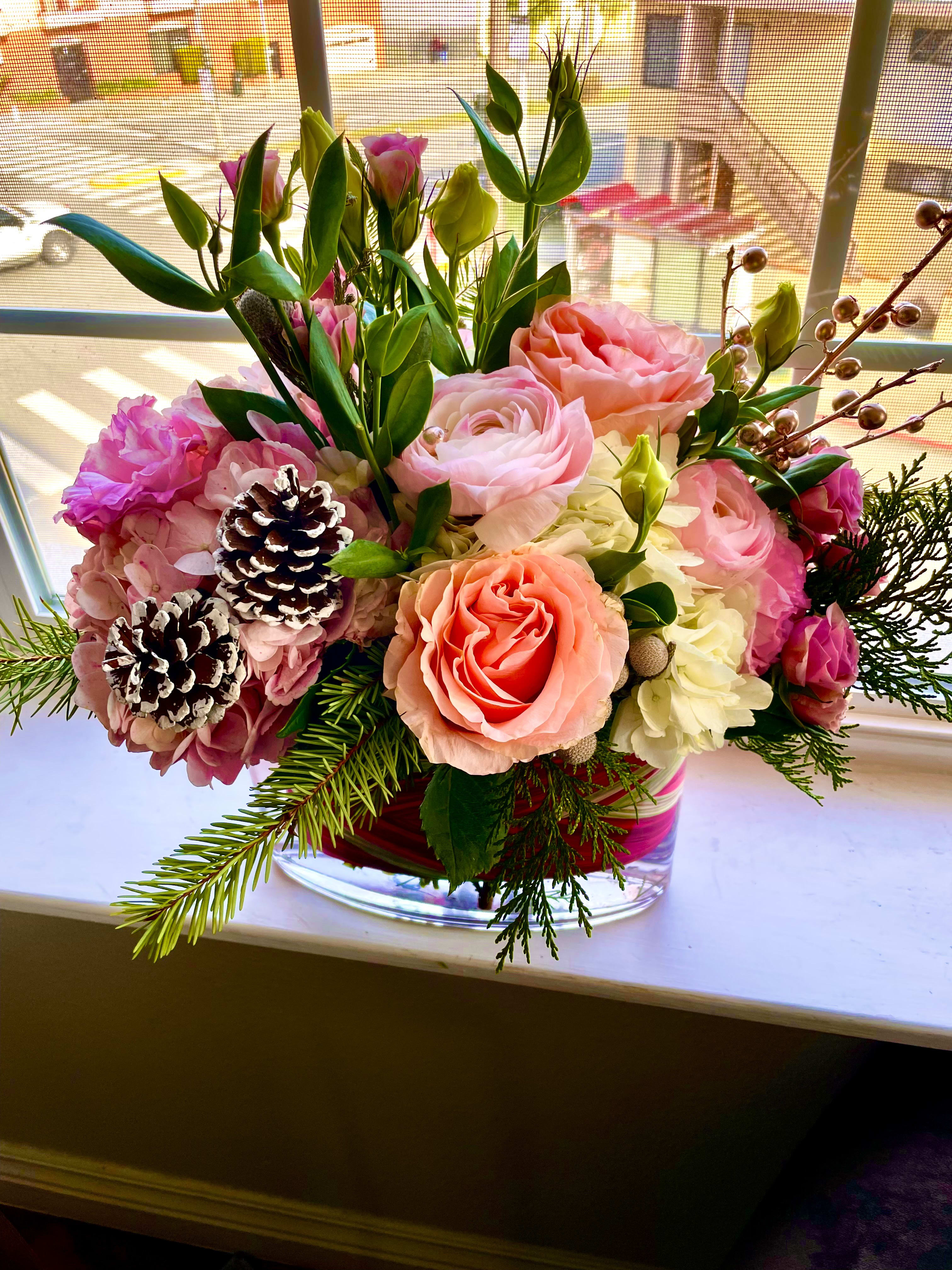 Pink and peach floral arrangement in a clear glass vase with pinecones