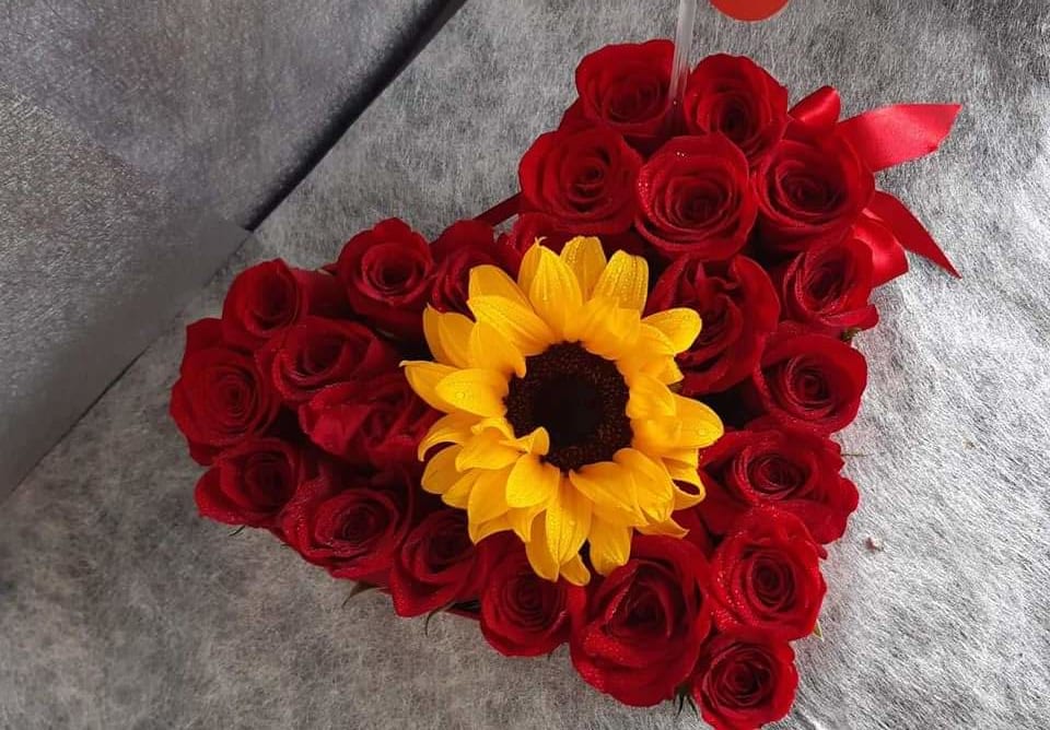 Heart-shaped bouquet of red roses with a yellow sunflower center